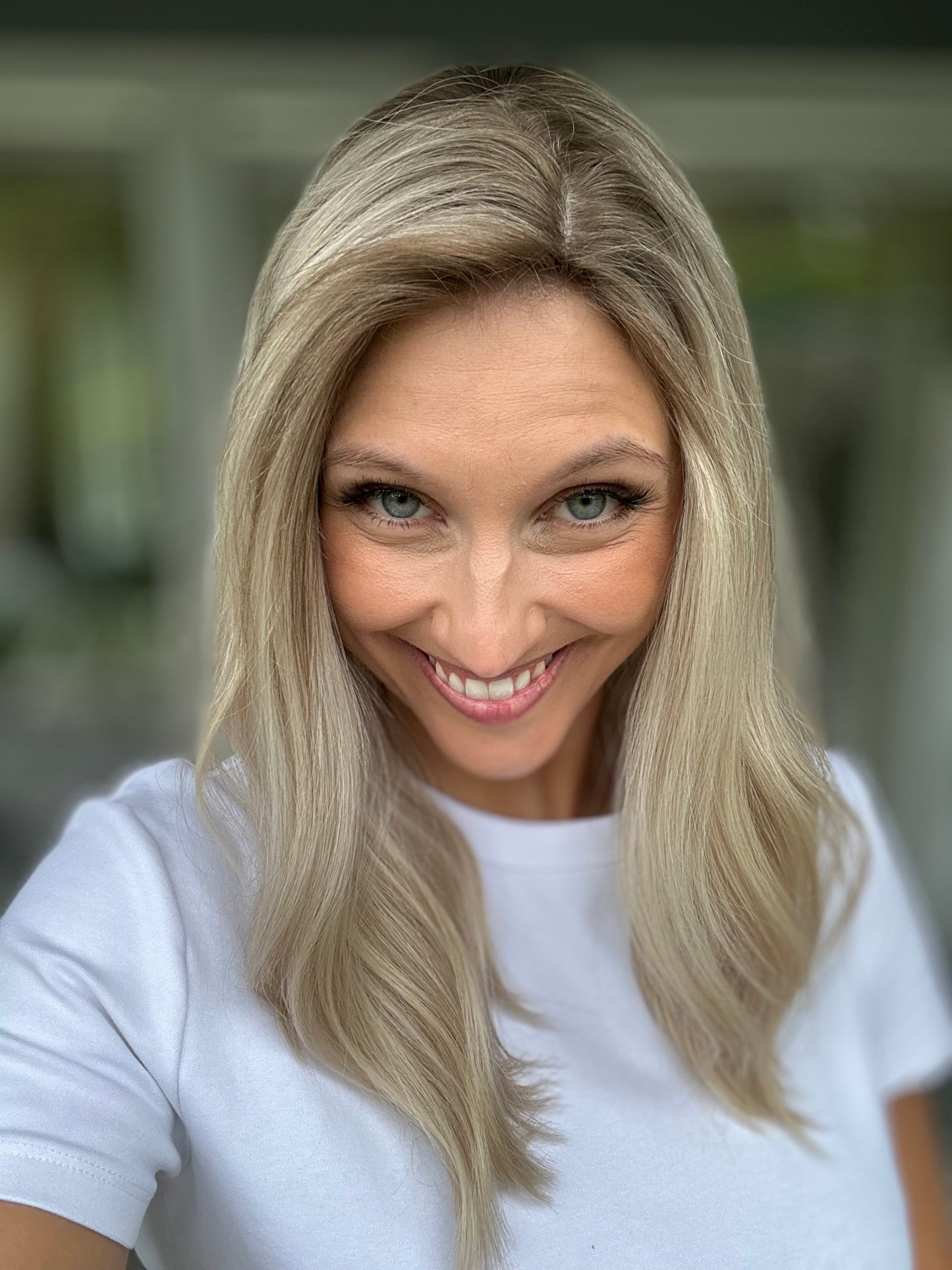 Bild zeigt attraktive Frau, die ihren Kopf leicht beugt, sodass blonder Haaransatz sichtbar wird. Bild dient der Produktpräsentation eines Artikels in der Kategorie Topper/Perücken.