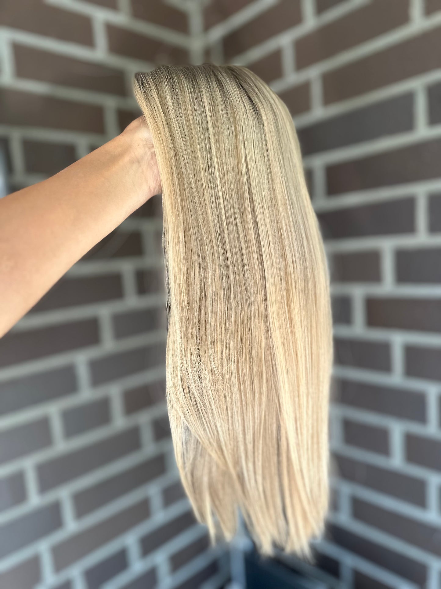 Bild zeigt blondes Echthaarteil, das seitlich ins Bild gehalten wird. Bild dient der Produktpräsentation eines Artikels in der Kategorie Topper/Perücken.