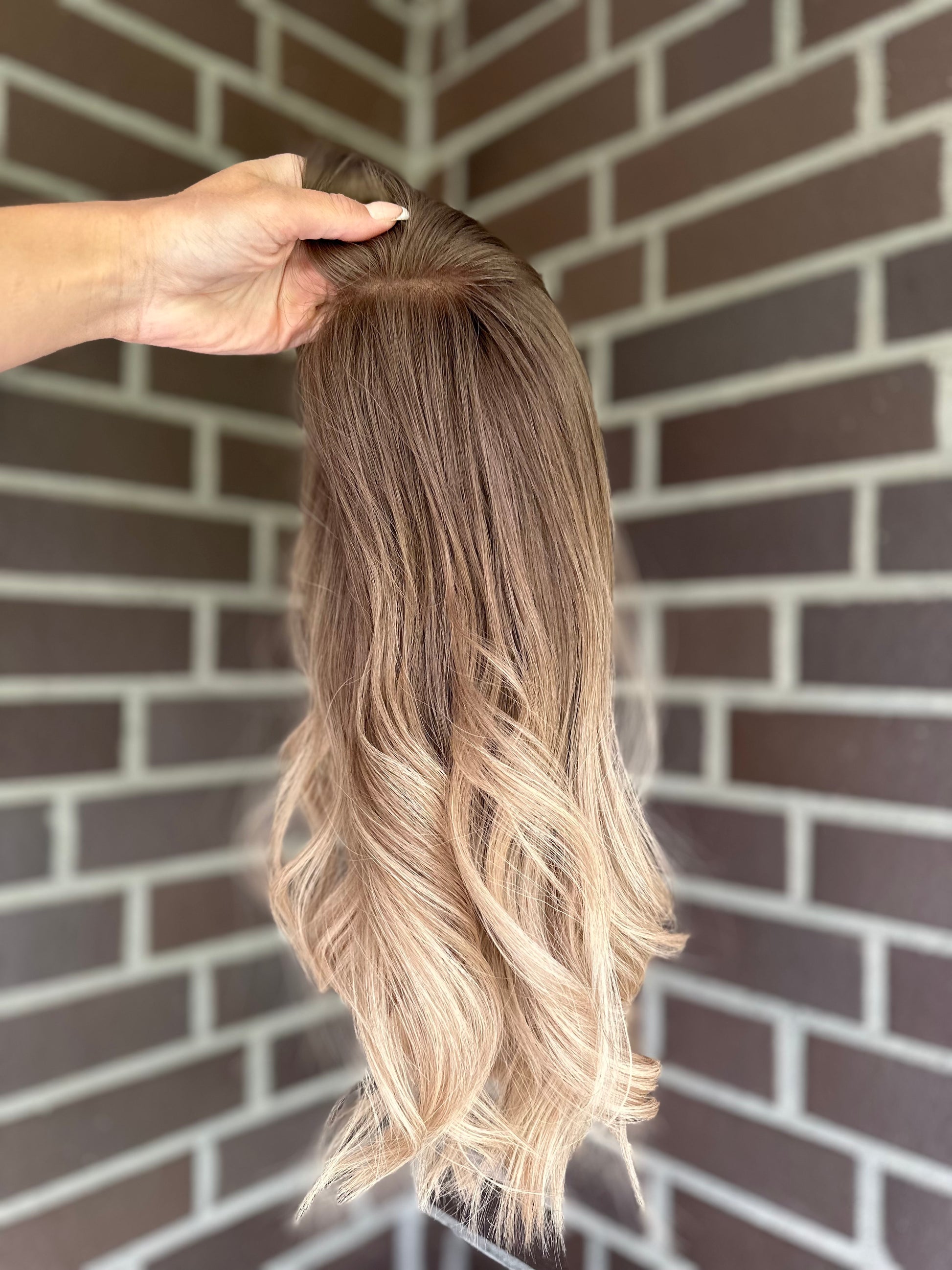 Bild zeigt blondes Echthaarteil, das seitlich ins Bild gehalten wird. Bild dient der Produktpräsentation eines Artikels in der Kategorie Topper/Perücken.