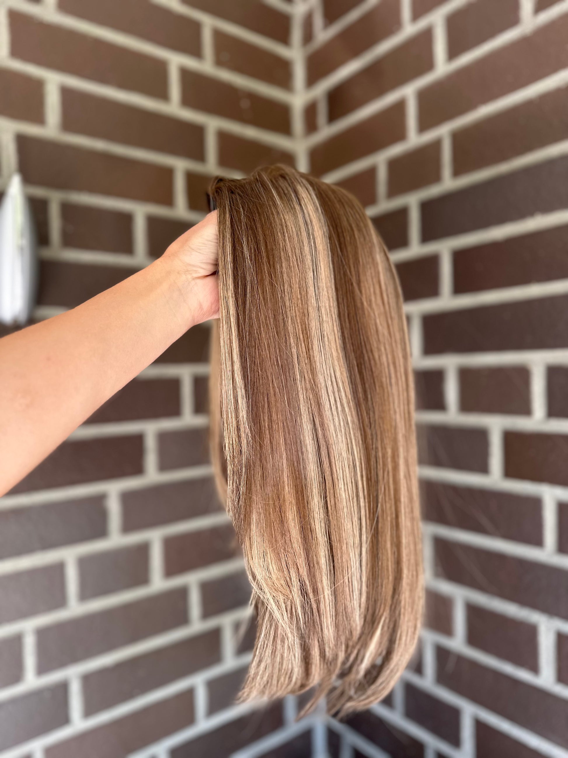 Bild zeigt blondes Echthaarteil, das seitlich ins Bild gehalten wird. Bild dient der Produktpräsentation eines Artikels in der Kategorie Topper/Perücken.