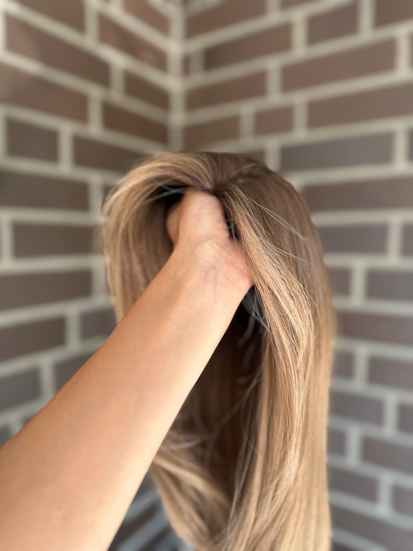 Bild zeigt blondes Echthaarteil, das seitlich ins Bild gehalten wird. Bild dient der Produktpräsentation eines Artikels in der Kategorie Topper/Perücken.