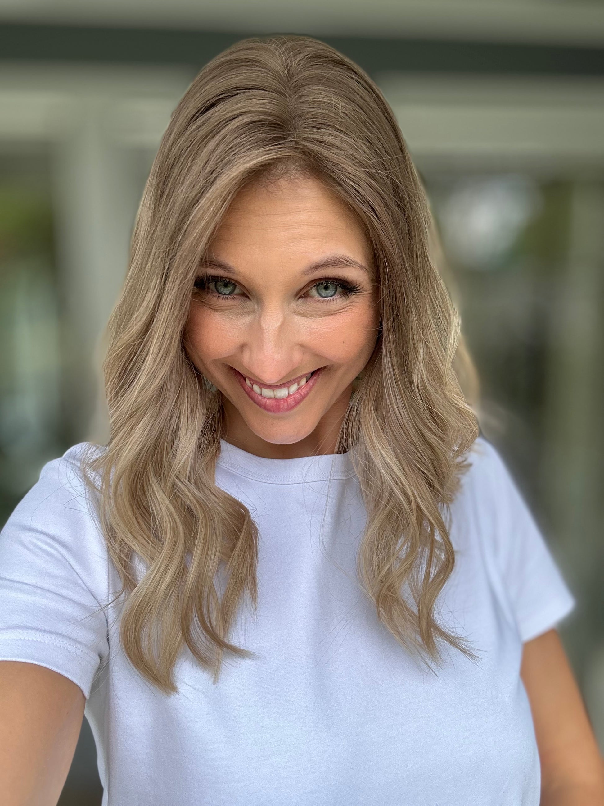 Bild zeigt attraktive Frau, die ihren Kopf leicht beugt, sodass blonder Haaransatz sichtbar wird. Bild dient der Produktpräsentation eines Artikels in der Kategorie Topper/Perücken.
