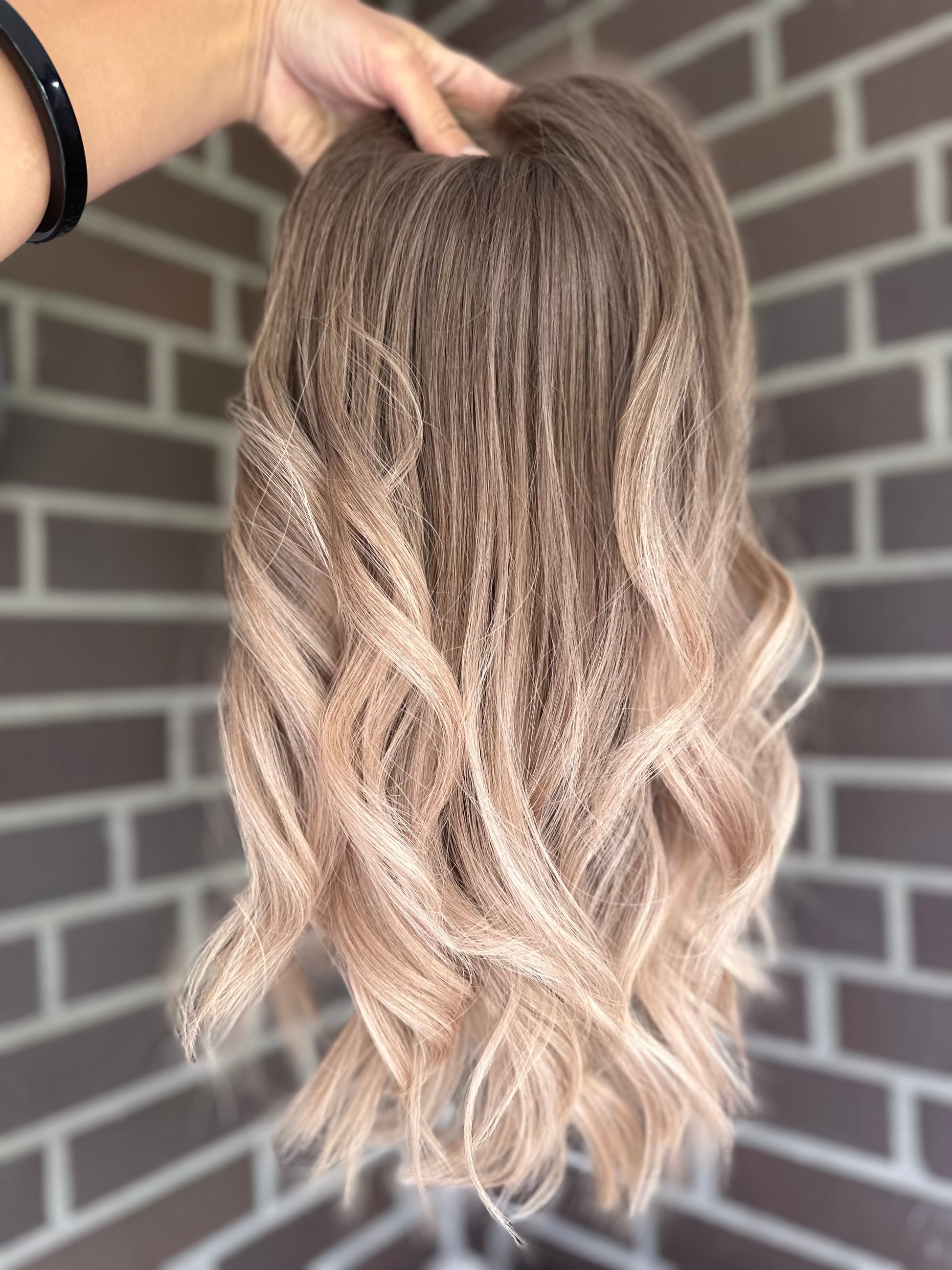 Bild zeigt blondes Echthaarteil, das frontal ins Bild gehalten wird. Bild dient der Produktpräsentation eines Artikels in der Kategorie Topper/Perücken.