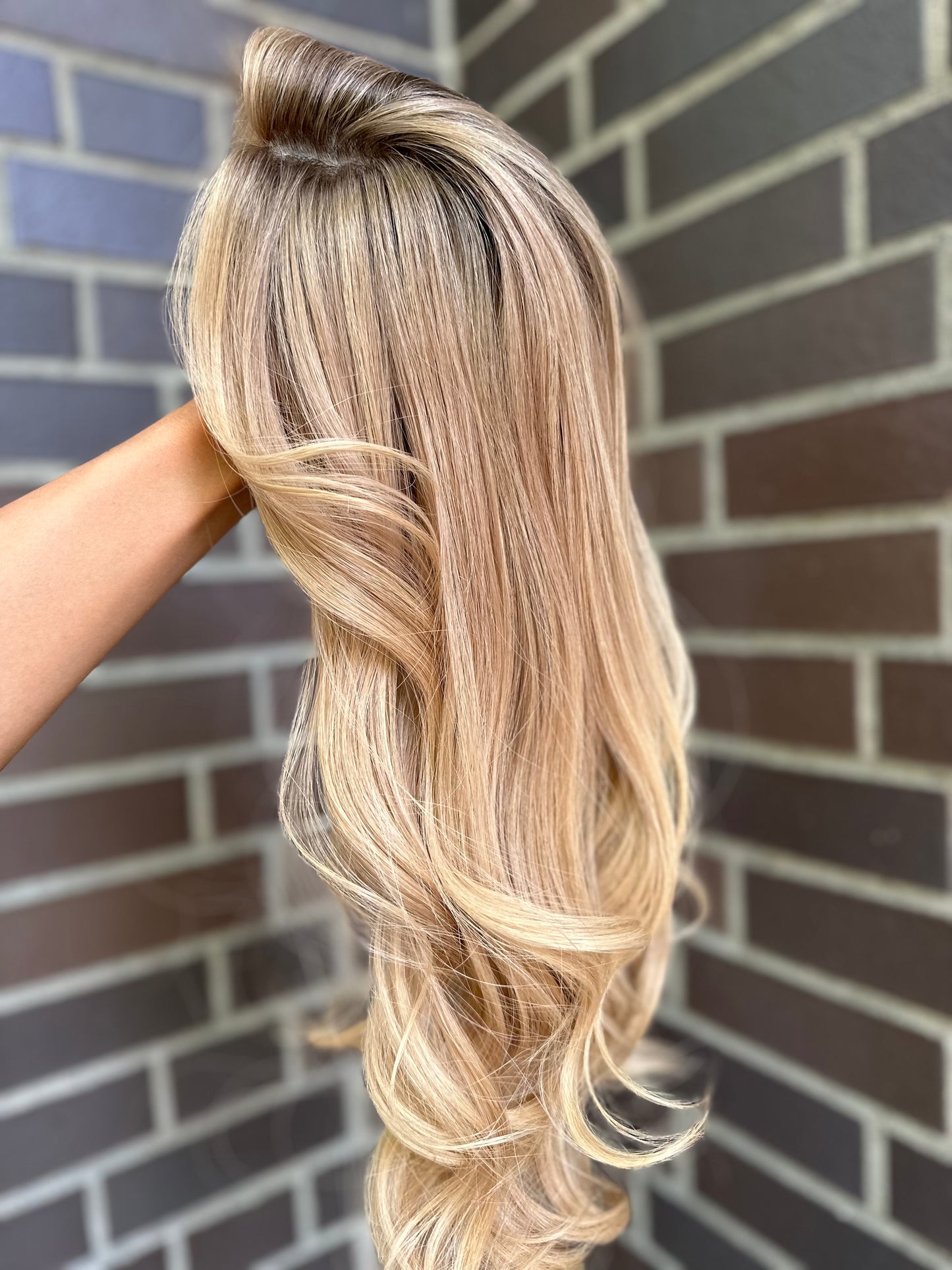 Bild zeigt blondes Echthaarteil, das seitlich ins Bild gehalten wird. Bild dient der Produktpräsentation eines Artikels in der Kategorie Topper/Perücken.