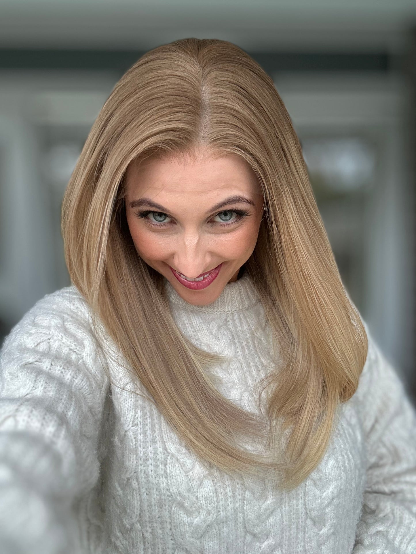 Bild zeigt attraktive Frau, die ihren Kopf leicht beugt, sodass blonder Haaransatz sichtbar wird. Bild dient der Produktpräsentation eines Artikels in der Kategorie Topper/Perücken.