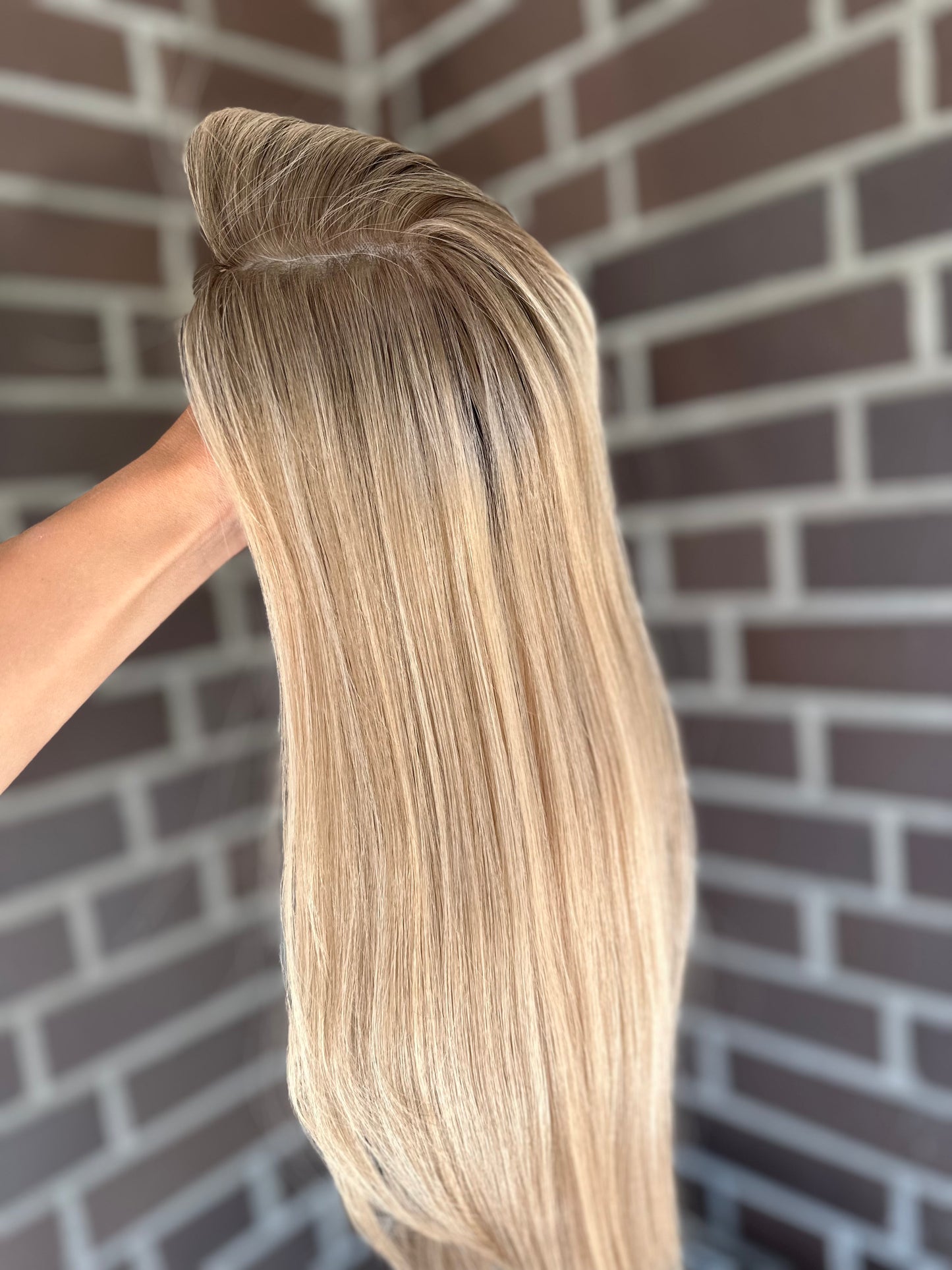 Bild zeigt blondes Echthaarteil, das seitlich ins Bild gehalten wird. Bild dient der Produktpräsentation eines Artikels in der Kategorie Topper/Perücken.