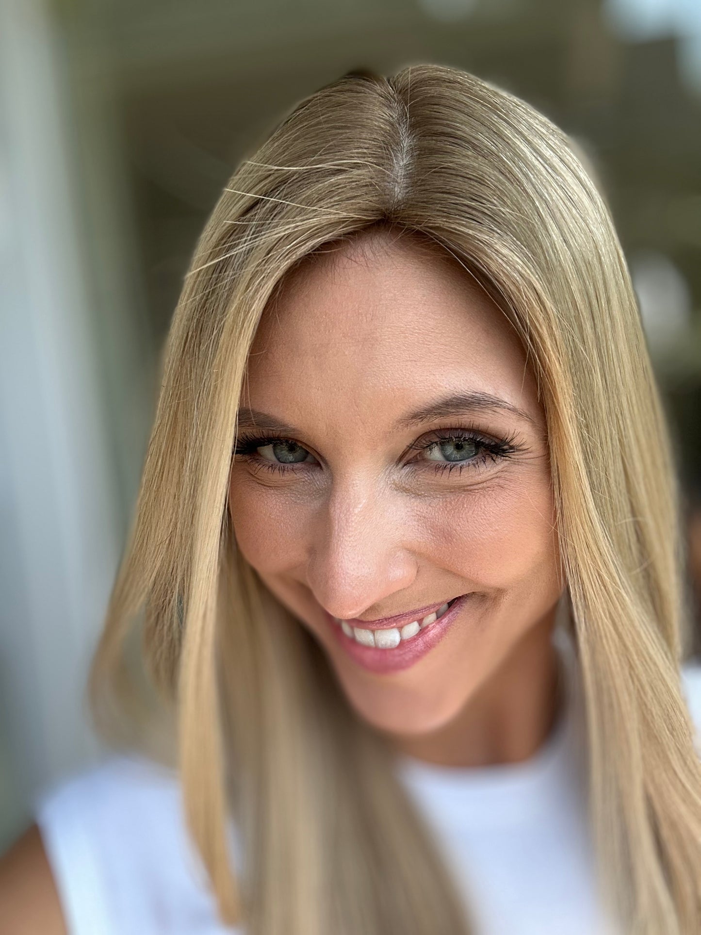 Bild zeigt attraktive Frau, die ihren Kopf leicht beugt, sodass blonder Haaransatz sichtbar wird. Bild dient der Produktpräsentation eines Artikels in der Kategorie Topper/Perücken.