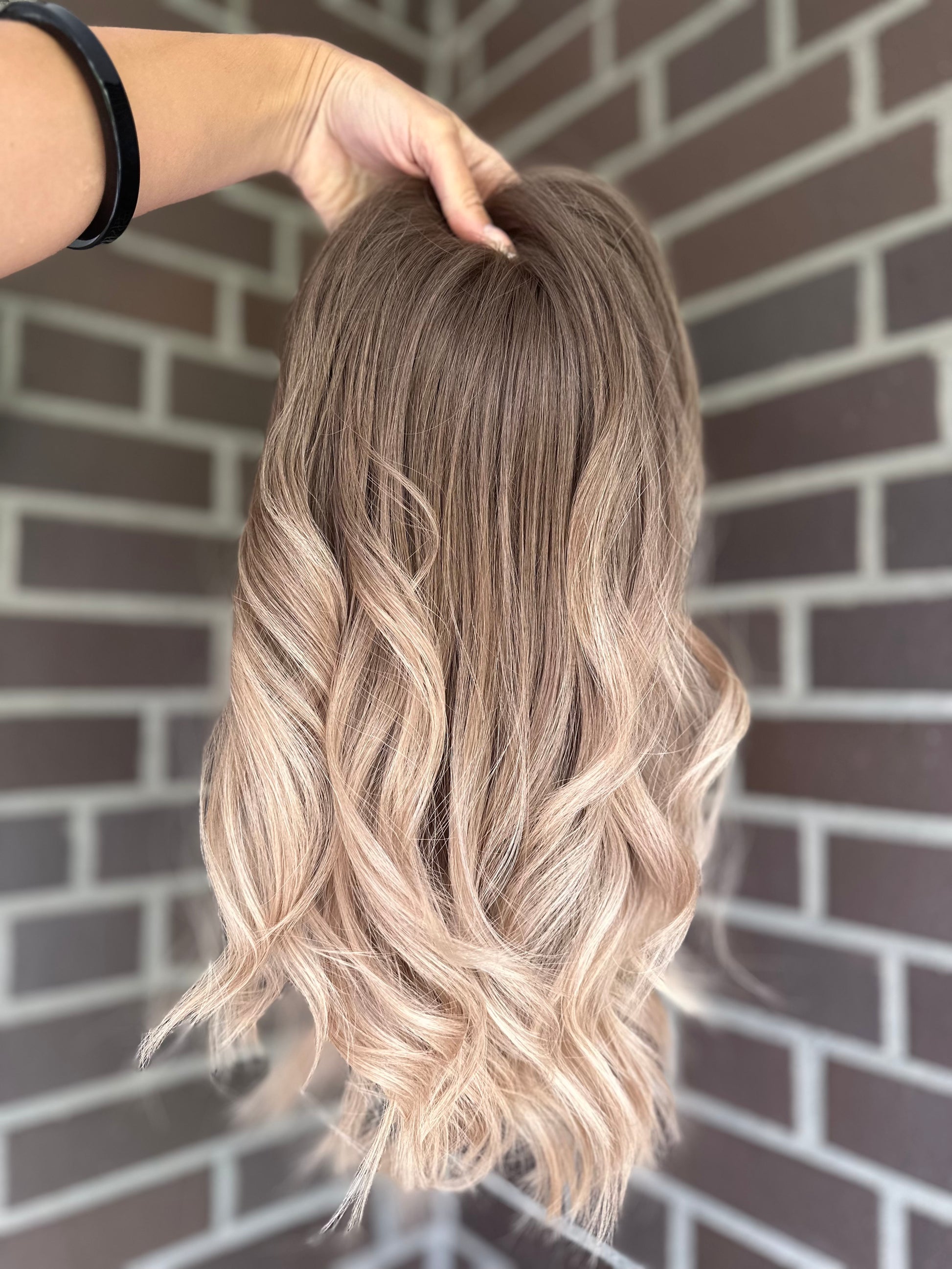 Bild zeigt blondes Echthaarteil, das frontal ins Bild gehalten wird. Bild dient der Produktpräsentation eines Artikels in der Kategorie Topper/Perücken.
