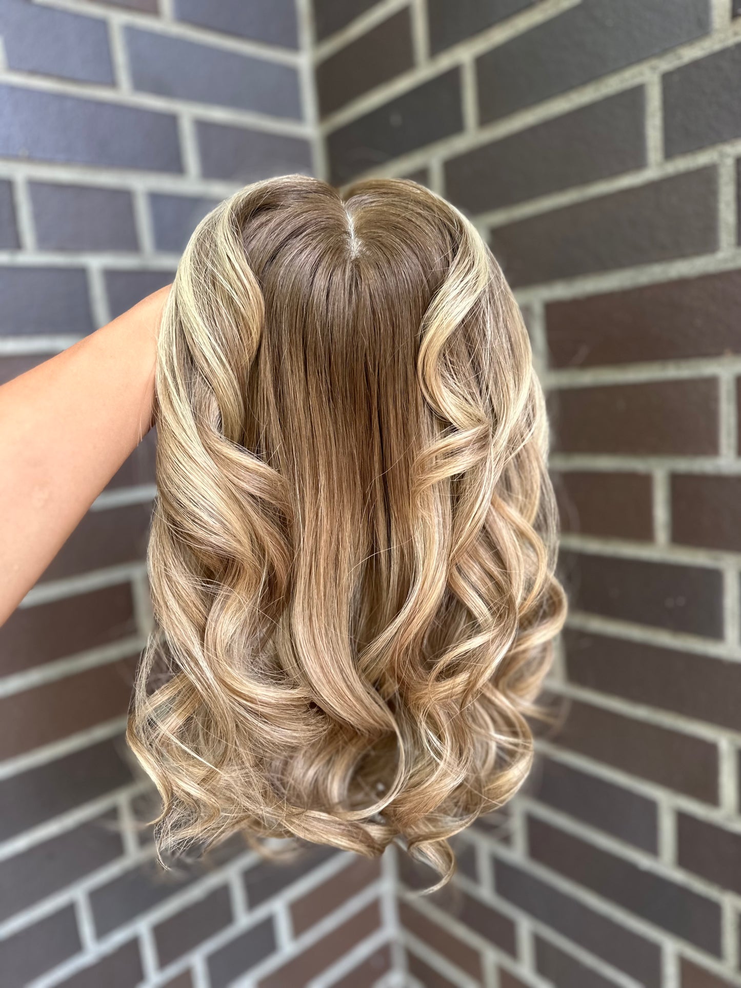 Bild zeigt blondes Echthaarteil, das frontal ins Bild gehalten wird. Bild dient der Produktpräsentation eines Artikels in der Kategorie Topper/Perücken.