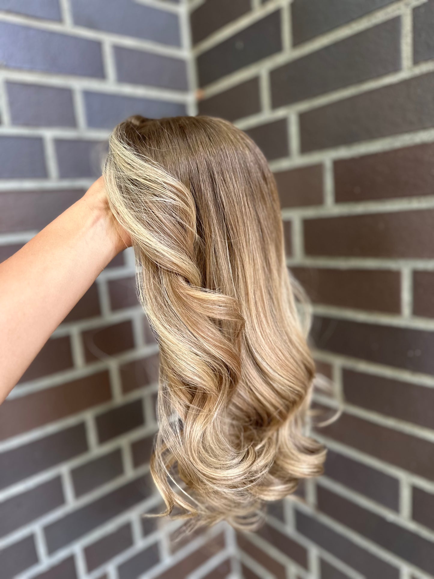 Bild zeigt blondes Echthaarteil, das seitlich ins Bild gehalten wird. Bild dient der Produktpräsentation eines Artikels in der Kategorie Topper/Perücken.