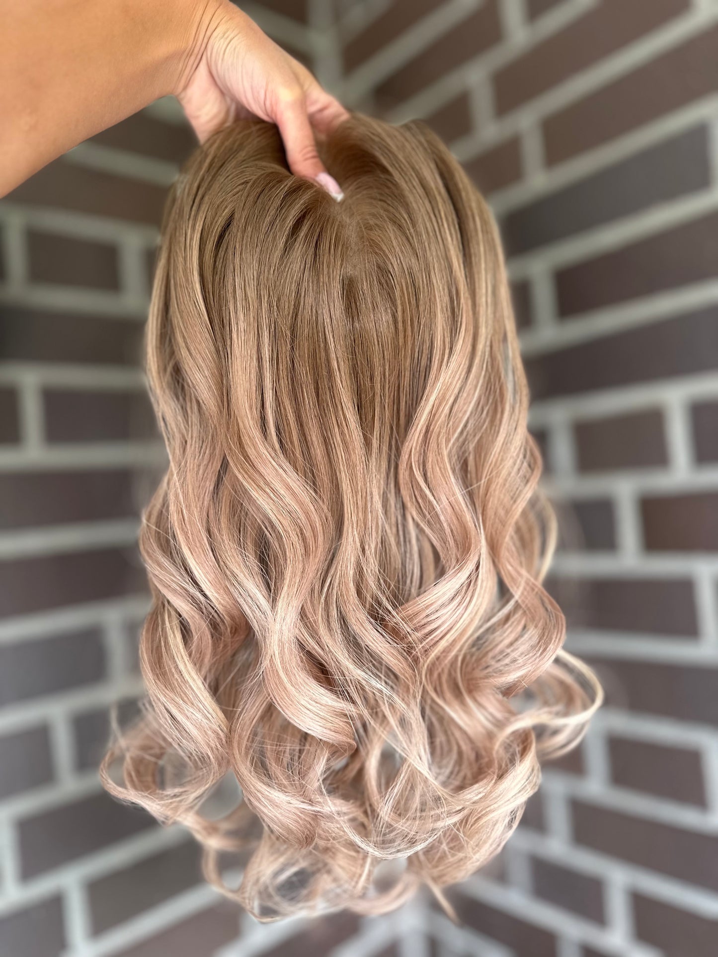 Bild zeigt blondes Echthaarteil, das frontal ins Bild gehalten wird. Bild dient der Produktpräsentation eines Artikels in der Kategorie Topper/Perücken.