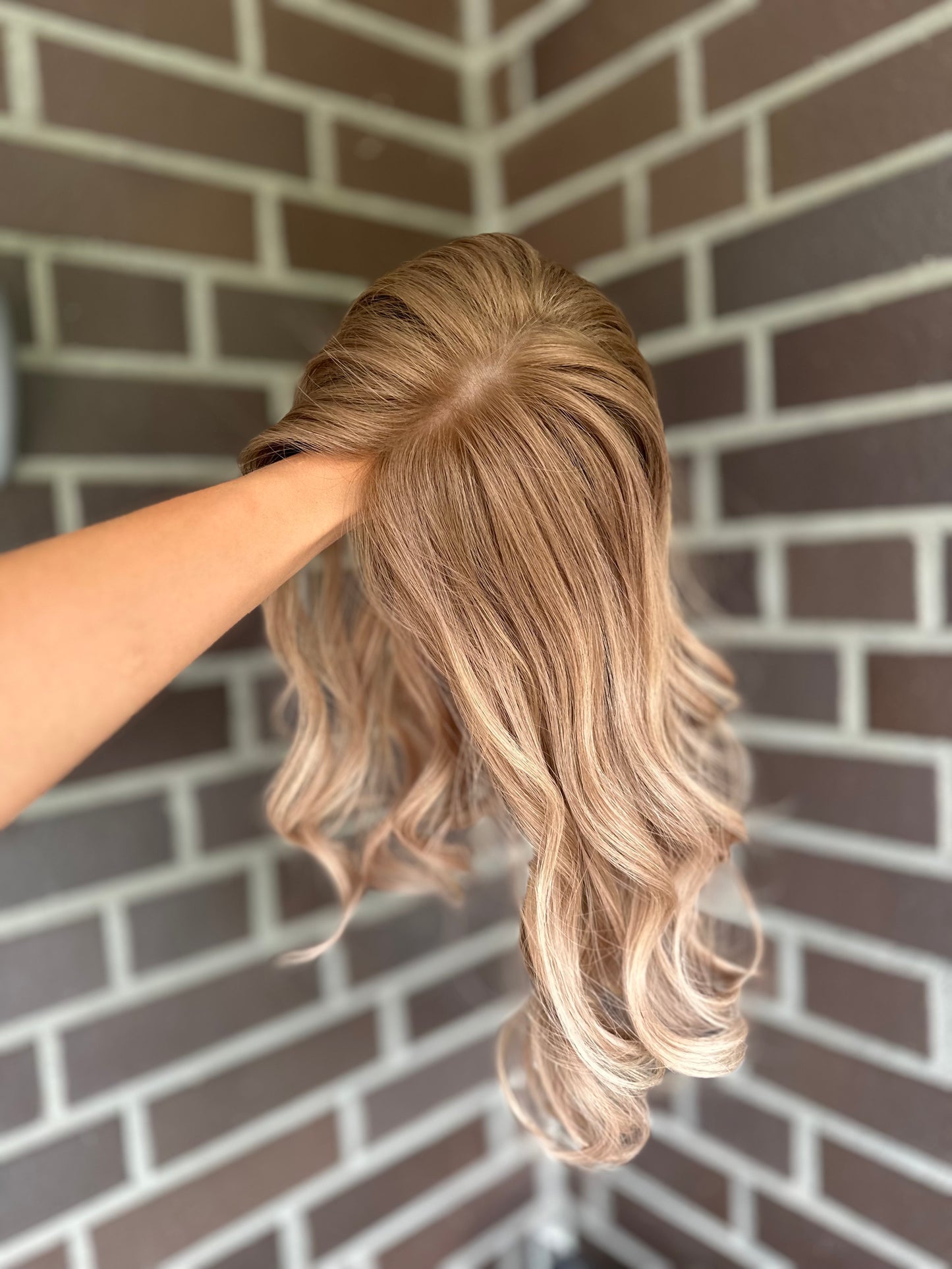 Bild zeigt blondes Echthaarteil, das seitlich ins Bild gehalten wird. Bild dient der Produktpräsentation eines Artikels in der Kategorie Topper/Perücken.