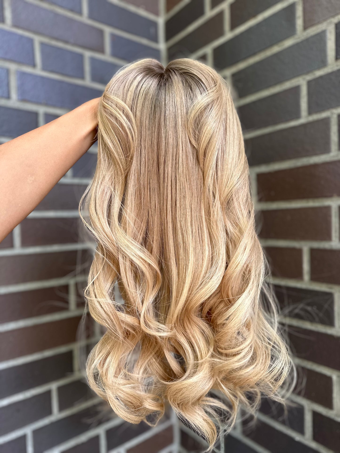 Bild zeigt blondes Echthaarteil, das frontal ins Bild gehalten wird. Bild dient der Produktpräsentation eines Artikels in der Kategorie Topper/Perücken.