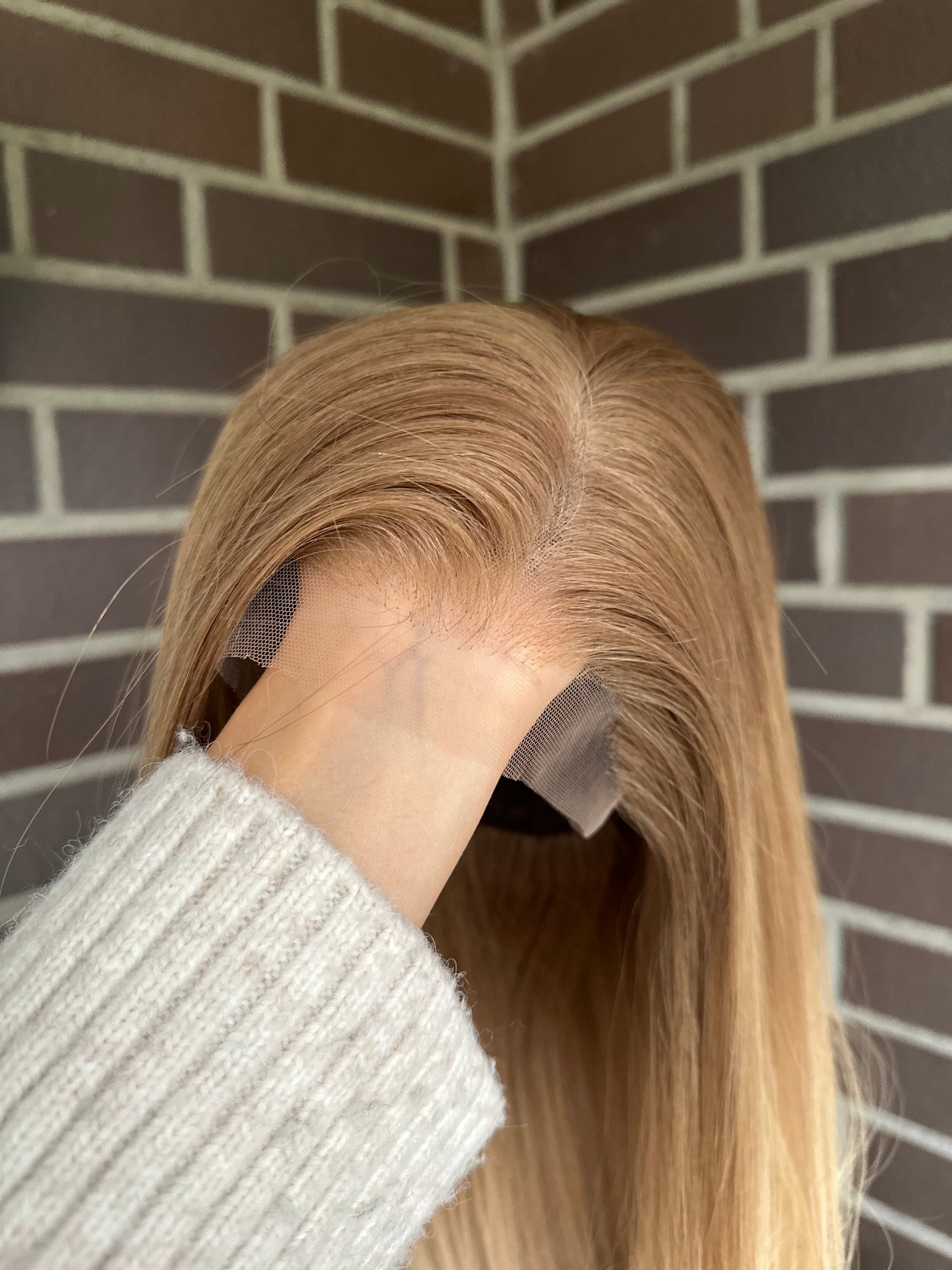 Bild zeigt blondes Echthaarteil, das frontal ins Bild gehalten wird. Bild dient der Produktpräsentation eines Artikels in der Kategorie Topper/Perücken.