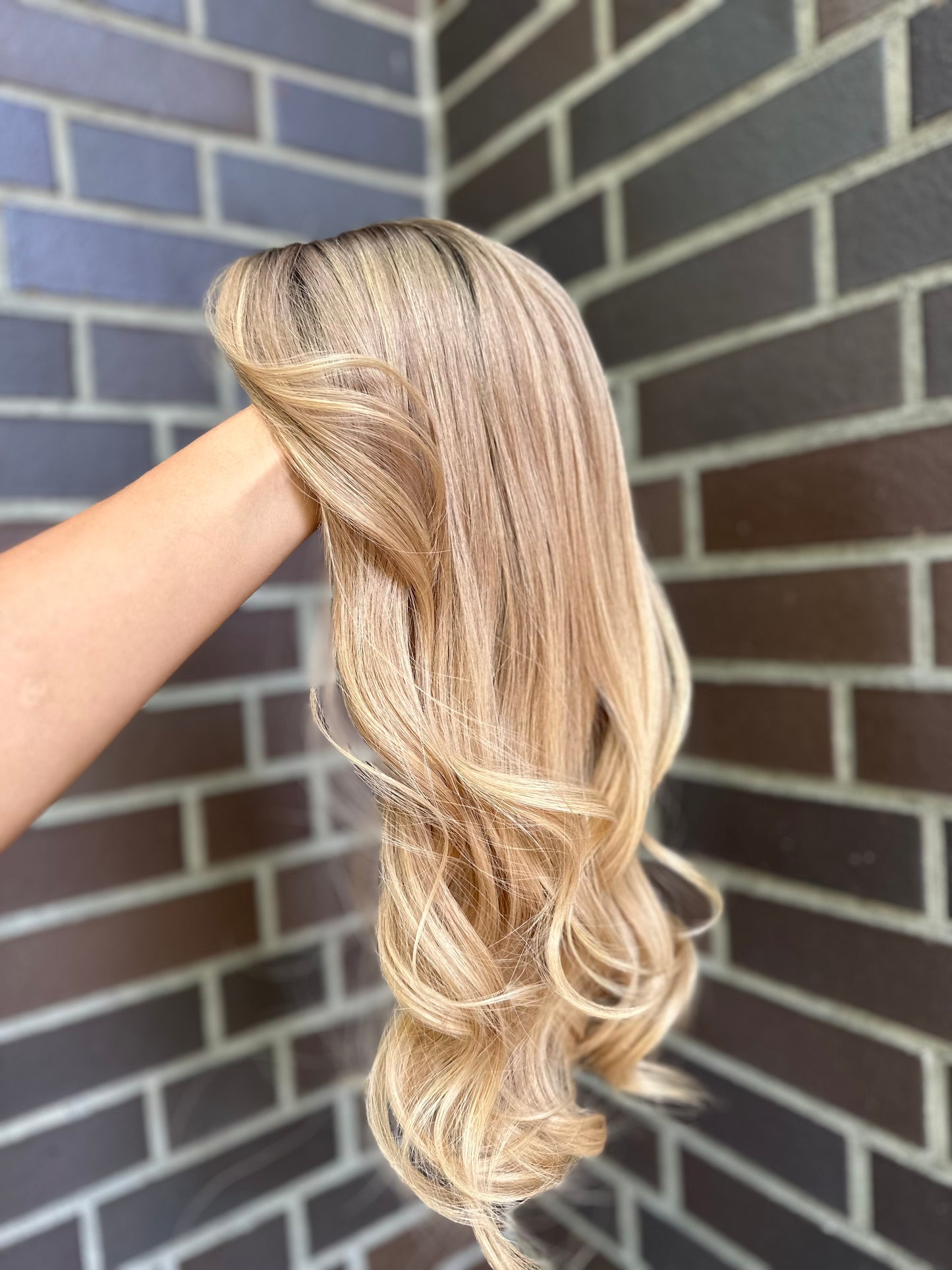 Bild zeigt blondes Echthaarteil, das seitlich ins Bild gehalten wird. Bild dient der Produktpräsentation eines Artikels in der Kategorie Topper/Perücken.