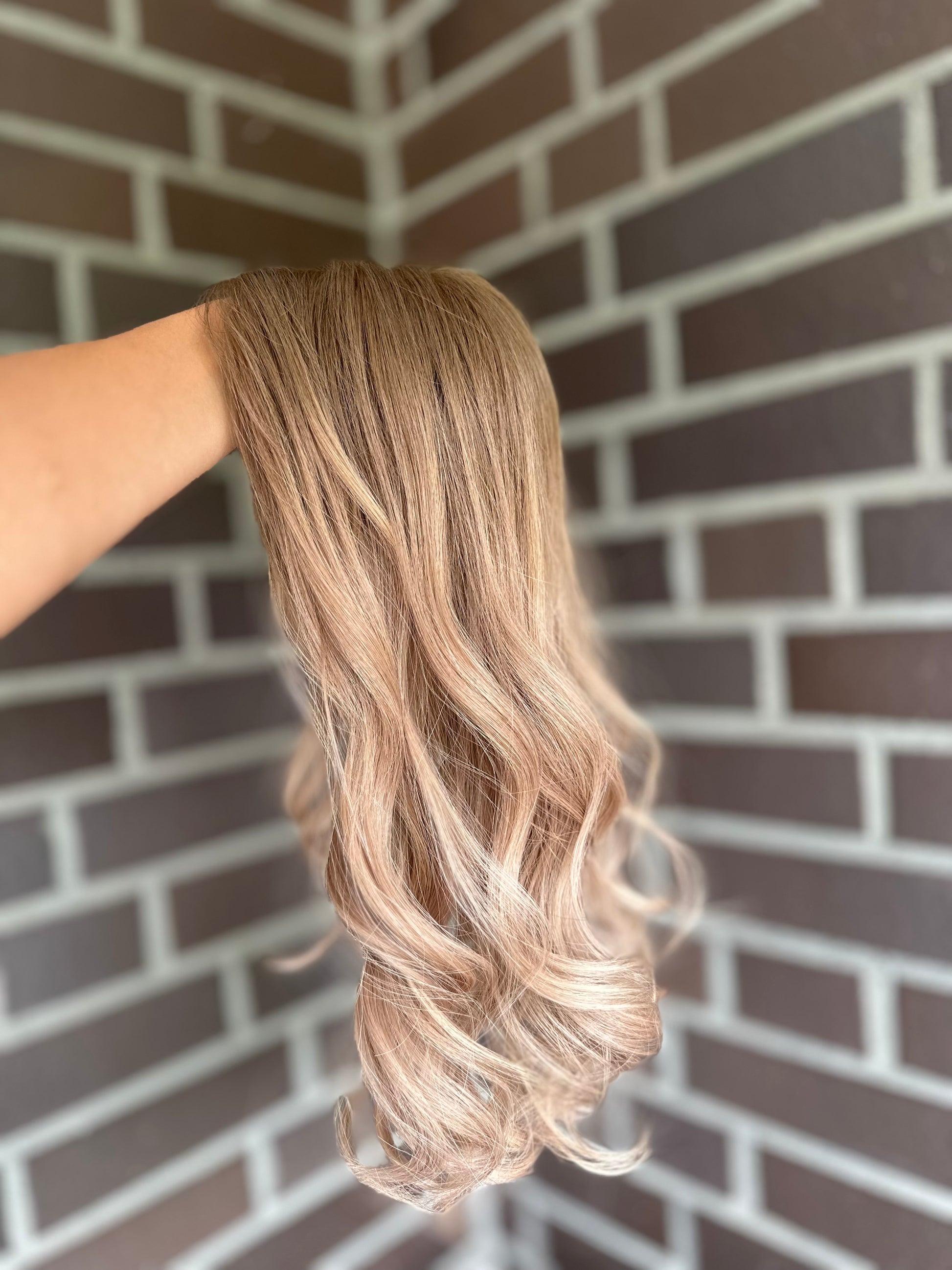 Bild zeigt blondes Echthaarteil, das seitlich ins Bild gehalten wird. Bild dient der Produktpräsentation eines Artikels in der Kategorie Topper/Perücken.