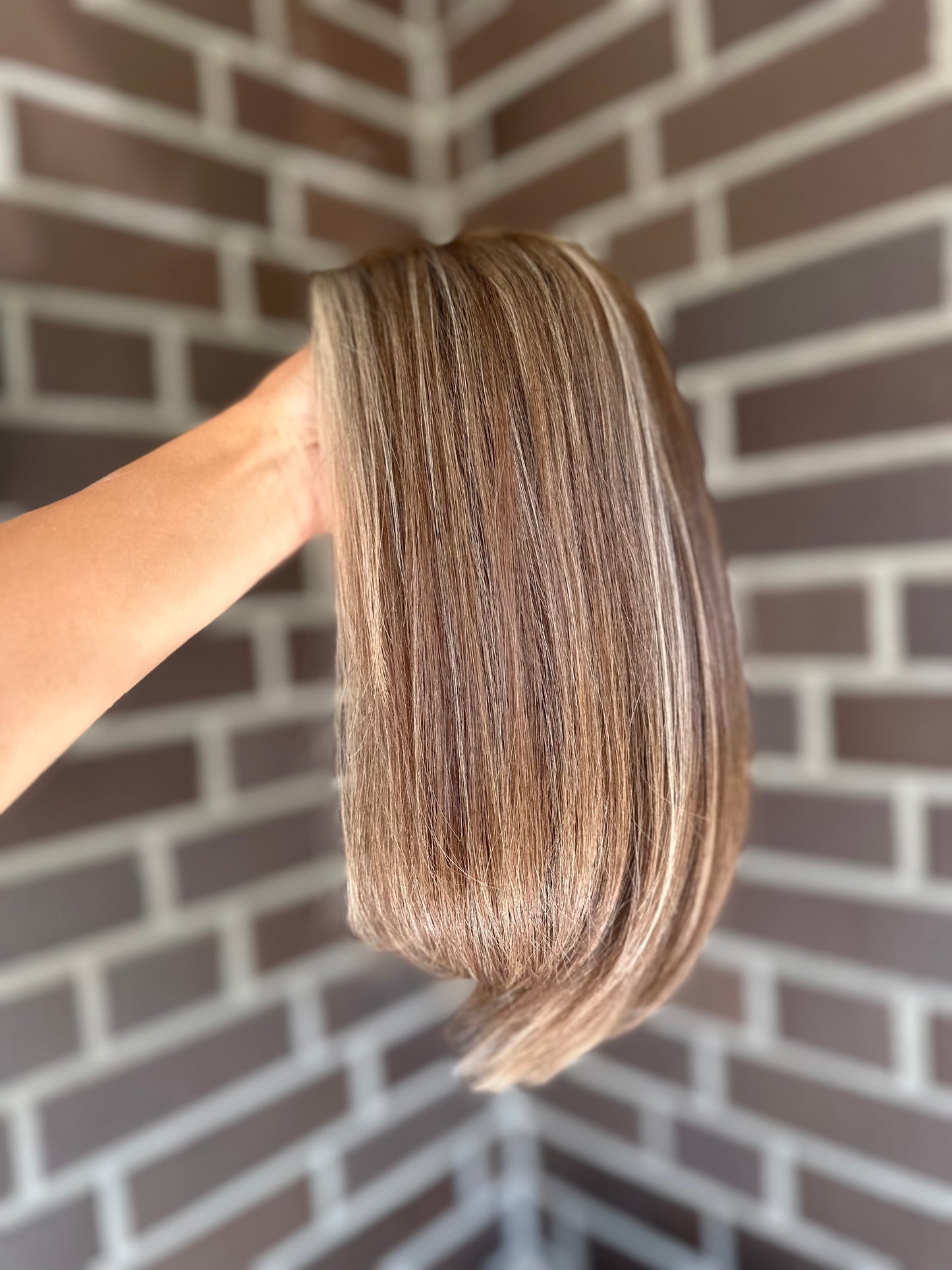 Bild zeigt blondes Echthaarteil, das seitlich ins Bild gehalten wird. Bild dient der Produktpräsentation eines Artikels in der Kategorie Topper/Perücken.