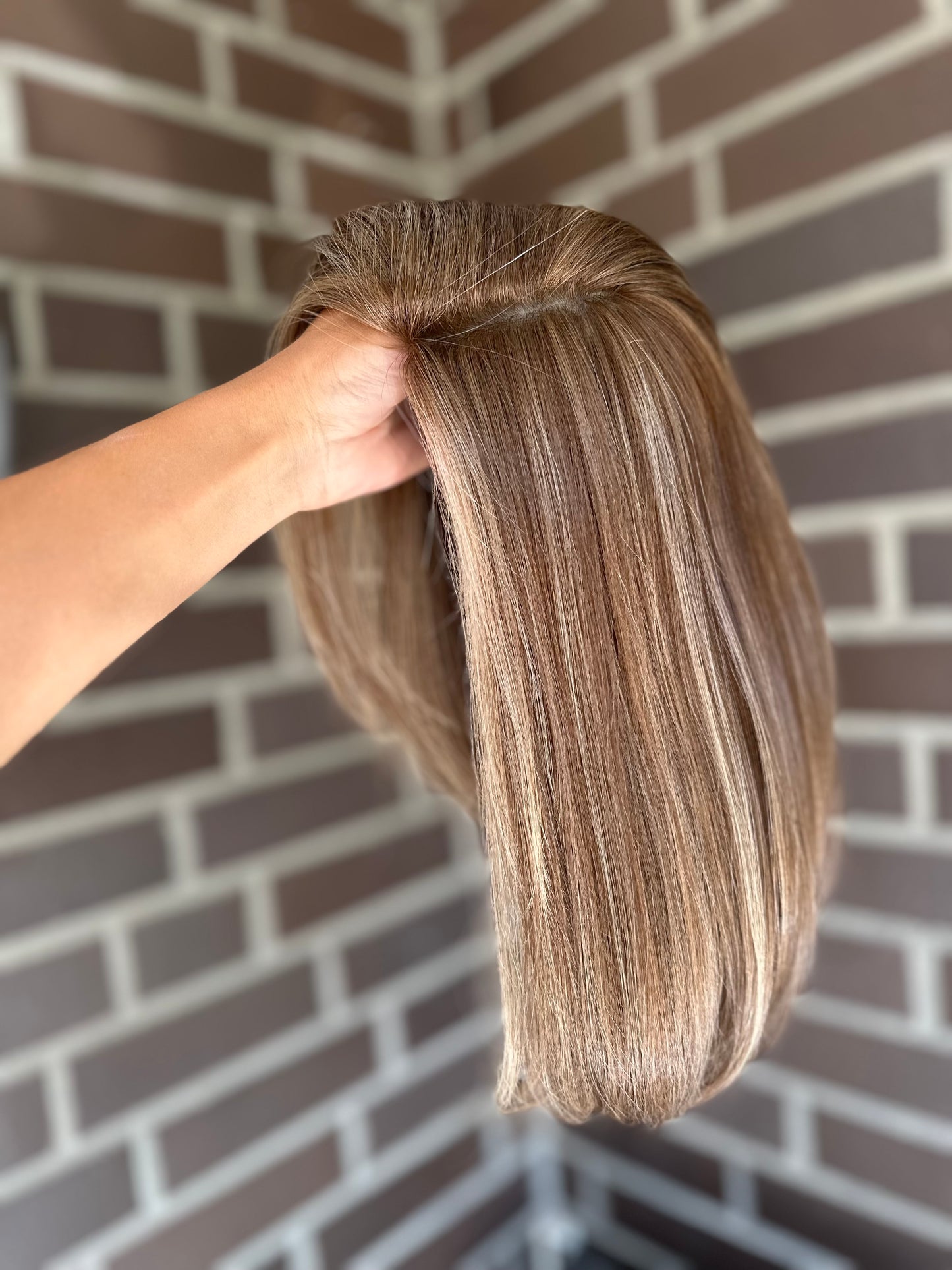 Bild zeigt blondes Echthaarteil, das seitlich ins Bild gehalten wird. Bild dient der Produktpräsentation eines Artikels in der Kategorie Topper/Perücken.