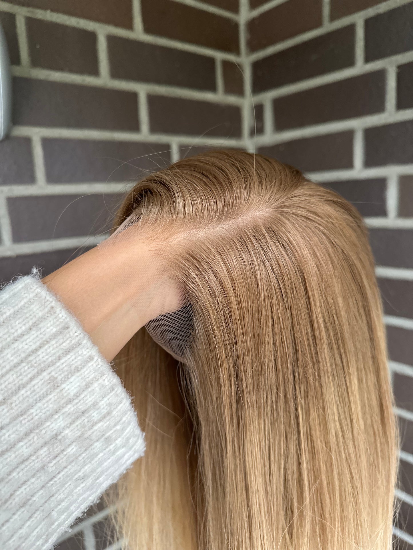 Bild zeigt blondes Echthaarteil, das seitlich ins Bild gehalten wird. Bild dient der Produktpräsentation eines Artikels in der Kategorie Topper/Perücken.