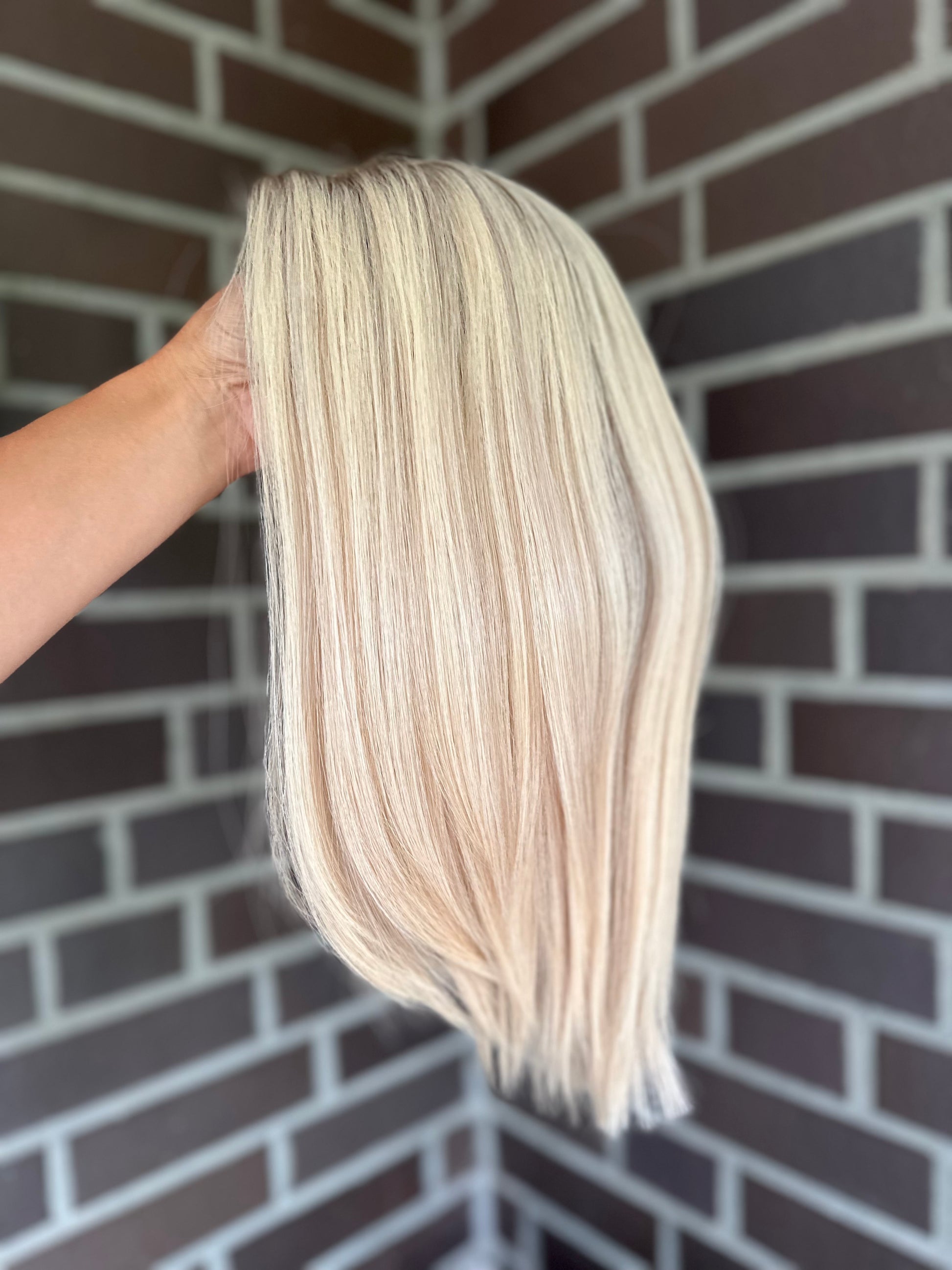 Bild zeigt blondes Echthaarteil, das seitlich ins Bild gehalten wird. Bild dient der Produktpräsentation eines Artikels in der Kategorie Topper/Perücken.