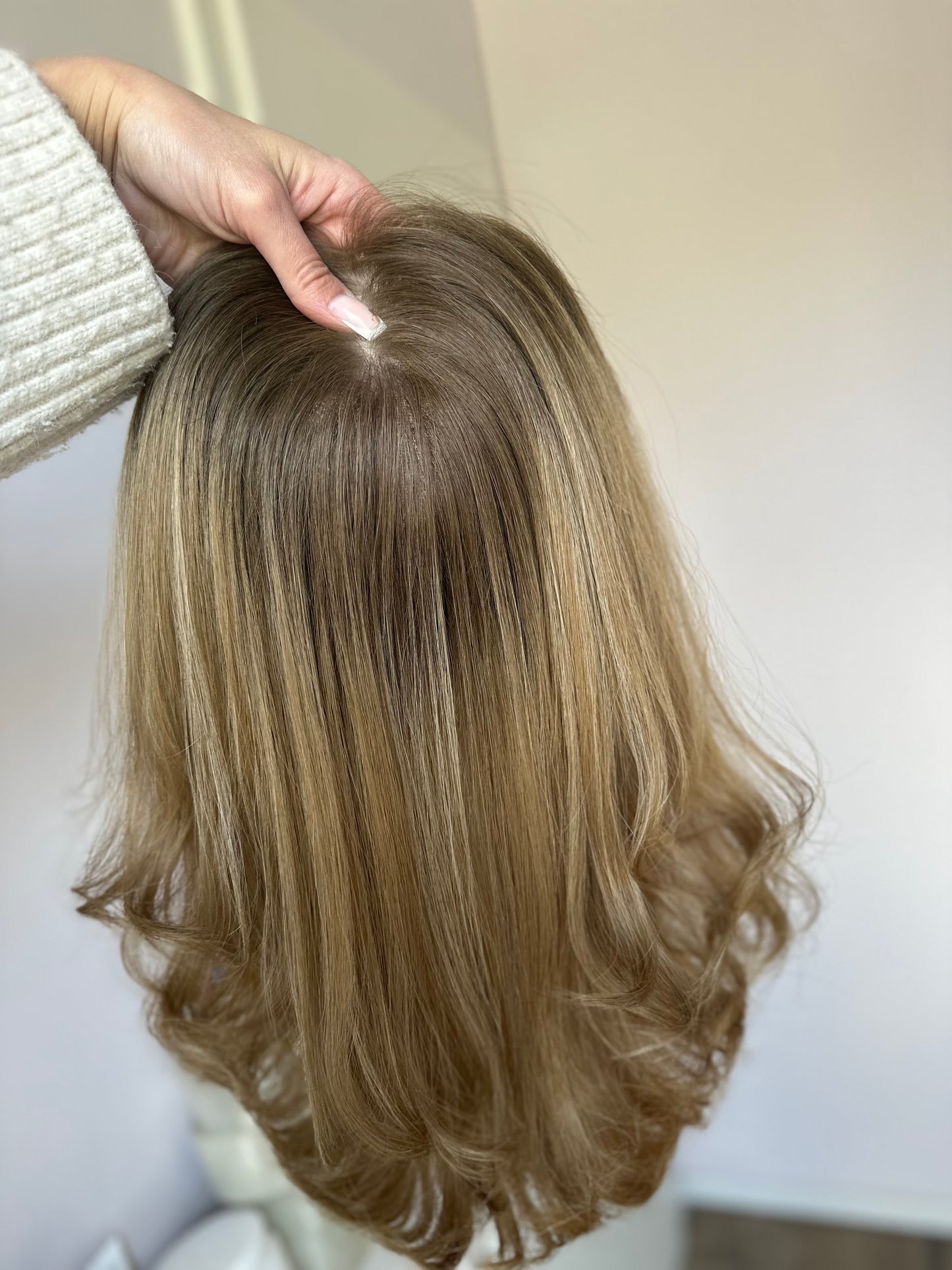 Bild zeigt blondes Echthaarteil, das frontal ins Bild gehalten wird. Bild dient der Produktpräsentation eines Artikels in der Kategorie Topper/Perücken.