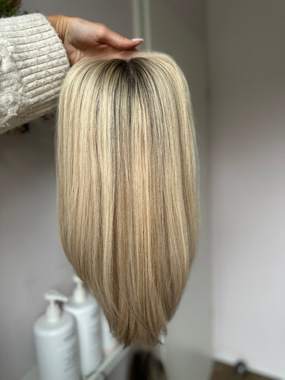 Bild zeigt blondes Echthaarteil, das frontal ins Bild gehalten wird. Bild dient der Produktpräsentation eines Artikels in der Kategorie Topper/Perücken.