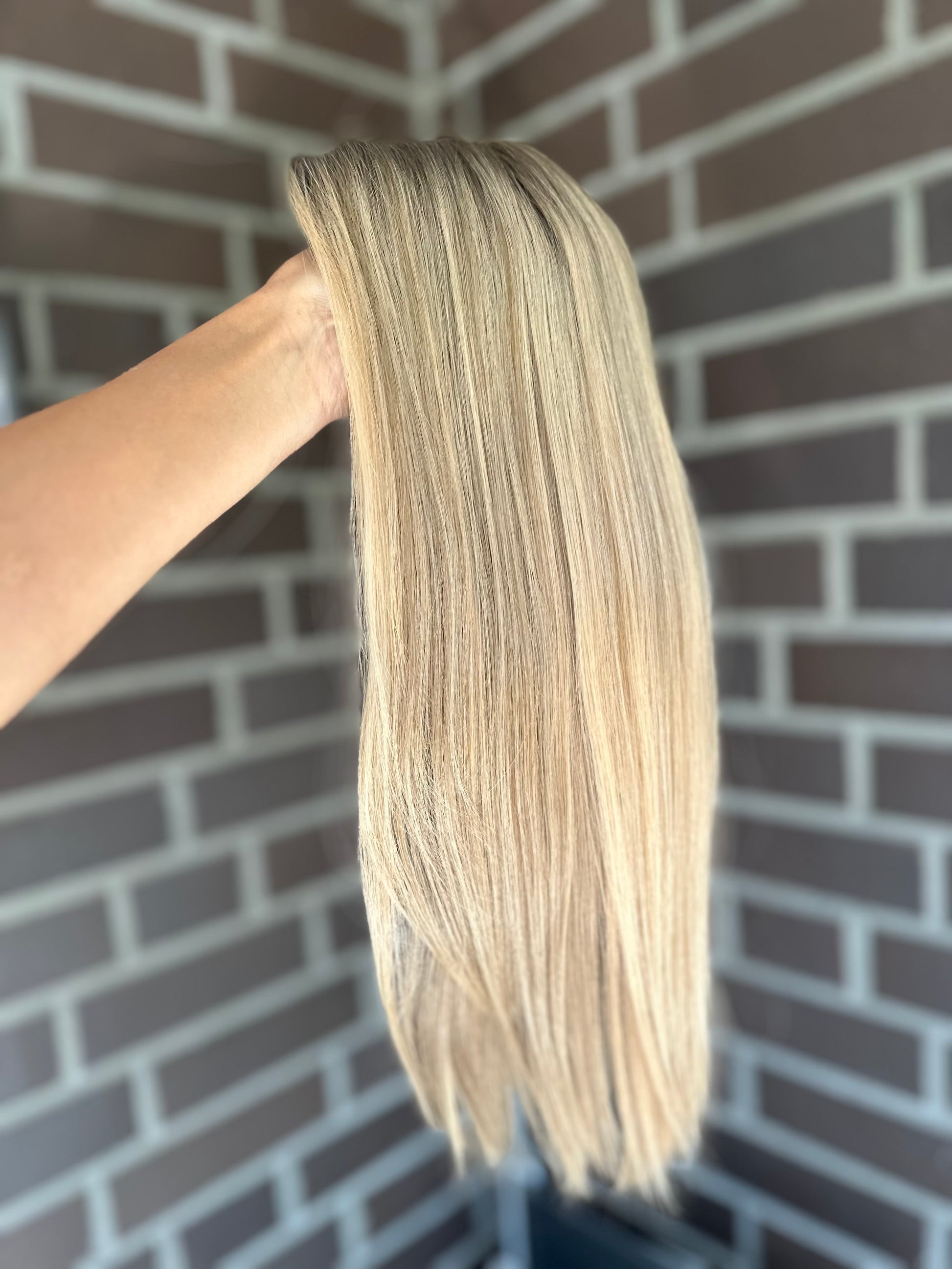 Bild zeigt blondes Echthaarteil, das seitlich ins Bild gehalten wird. Bild dient der Produktpräsentation eines Artikels in der Kategorie Topper/Perücken.