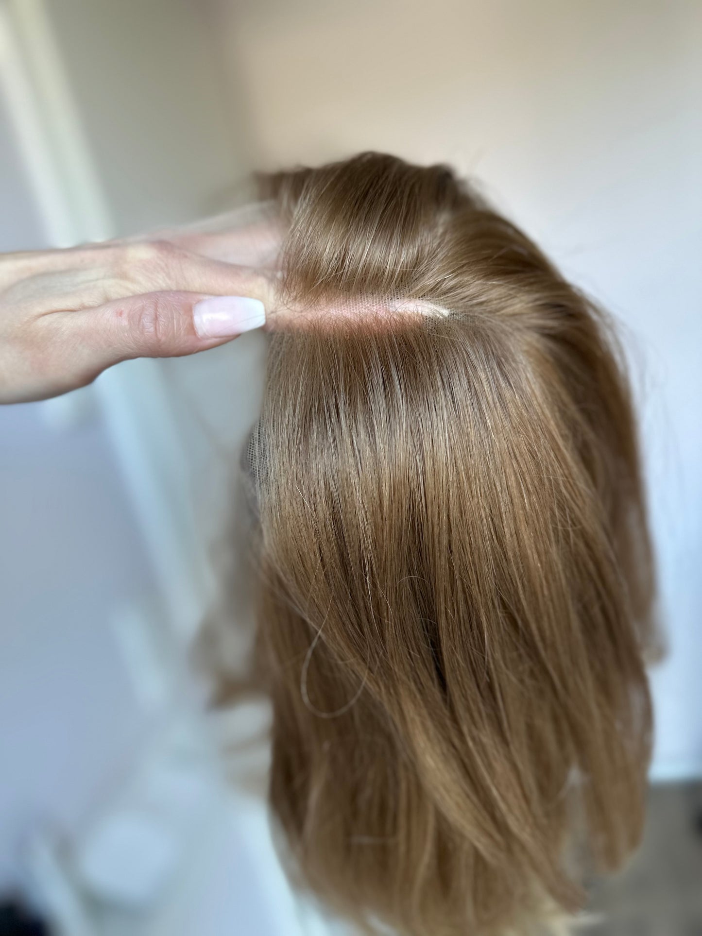Bild zeigt blondes Echthaarteil, das seitlich ins Bild gehalten wird. Bild dient der Produktpräsentation eines Artikels in der Kategorie Topper/Perücken.