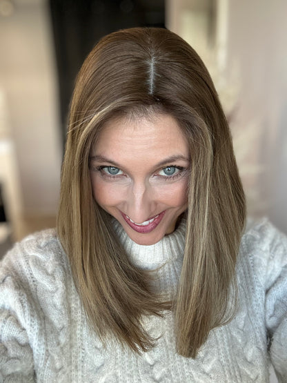 Bild zeigt attraktive Frau, die ihren Kopf leicht beugt, sodass brauner Haaransatz sichtbar wird. Bild dient der Produktpräsentation eines Artikels in der Kategorie Topper/Perücken.