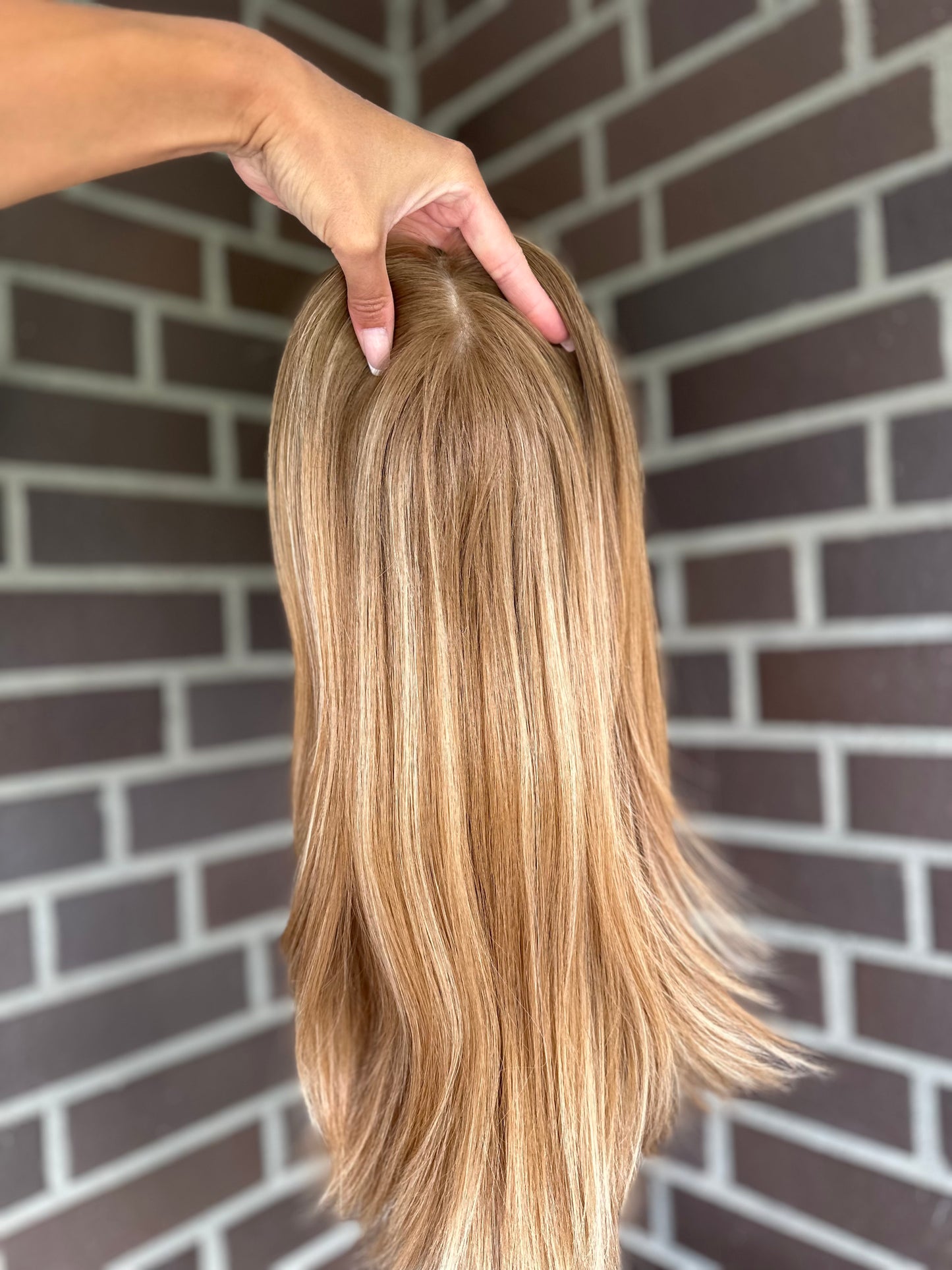 Bild zeigt blondes Echthaarteil, das frontal ins Bild gehalten wird. Bild dient der Produktpräsentation eines Artikels in der Kategorie Topper/Perücken.