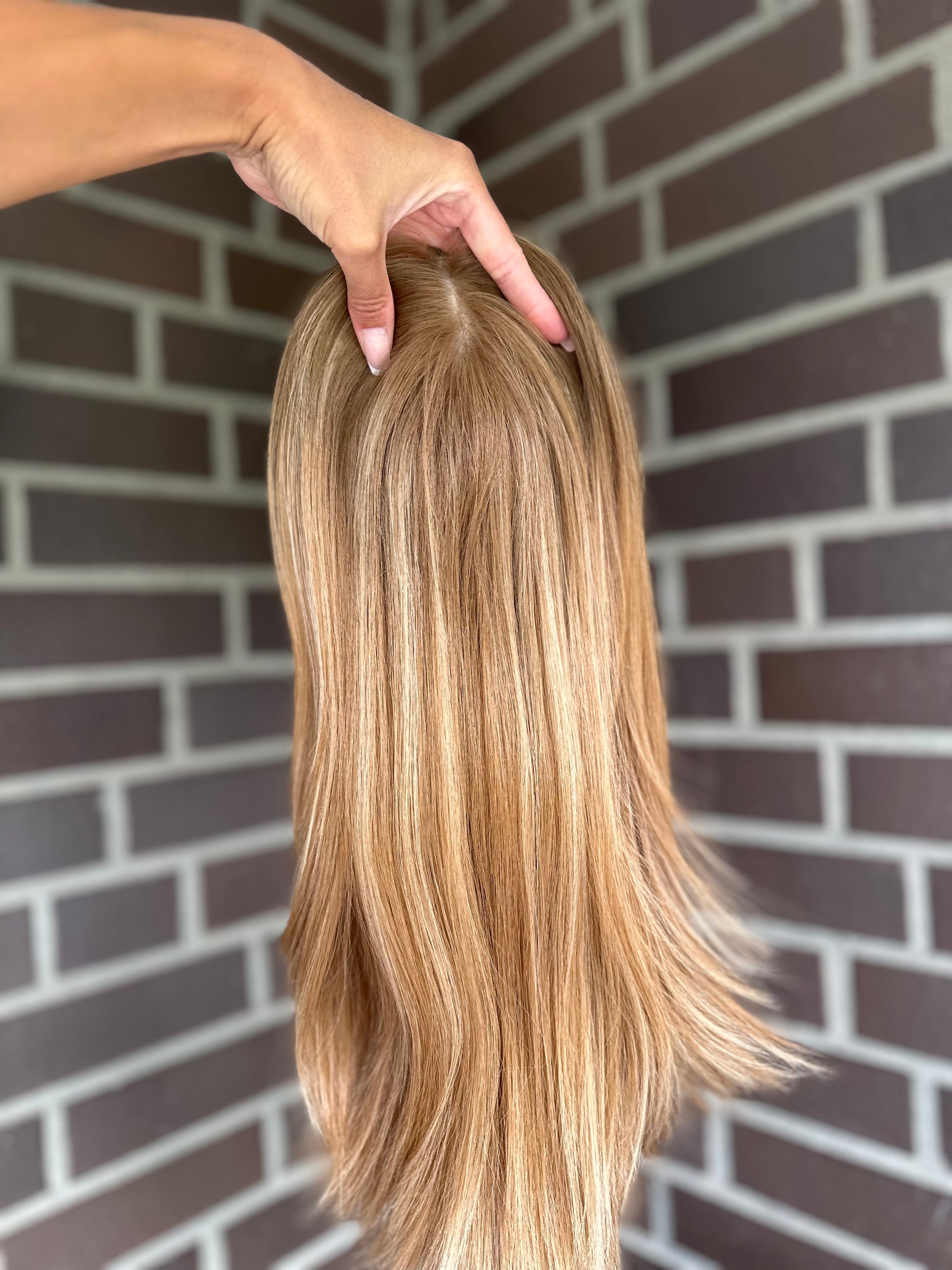 Bild zeigt blondes Echthaarteil, das frontal ins Bild gehalten wird. Bild dient der Produktpräsentation eines Artikels in der Kategorie Topper/Perücken.