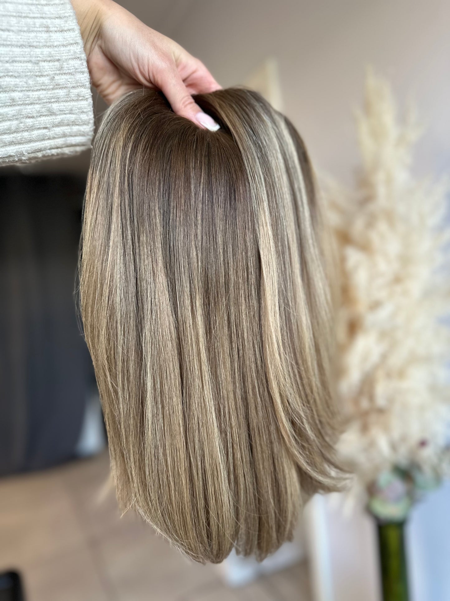 Bild zeigt blondes Echthaarteil, das frontal ins Bild gehalten wird. Bild dient der Produktpräsentation eines Artikels in der Kategorie Topper/Perücken.