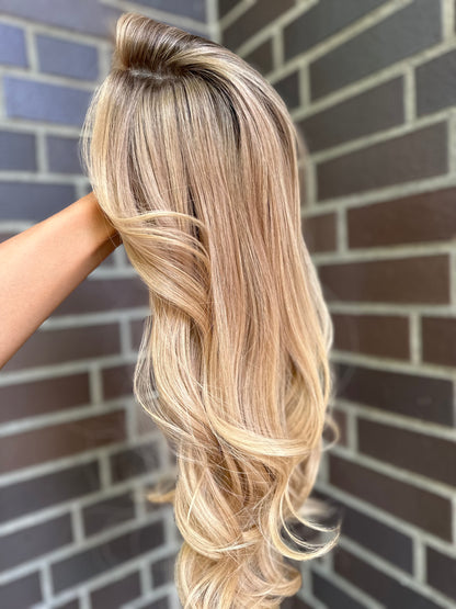 Bild zeigt blondes Echthaarteil, das seitlich ins Bild gehalten wird. Bild dient der Produktpräsentation eines Artikels in der Kategorie Topper/Perücken.