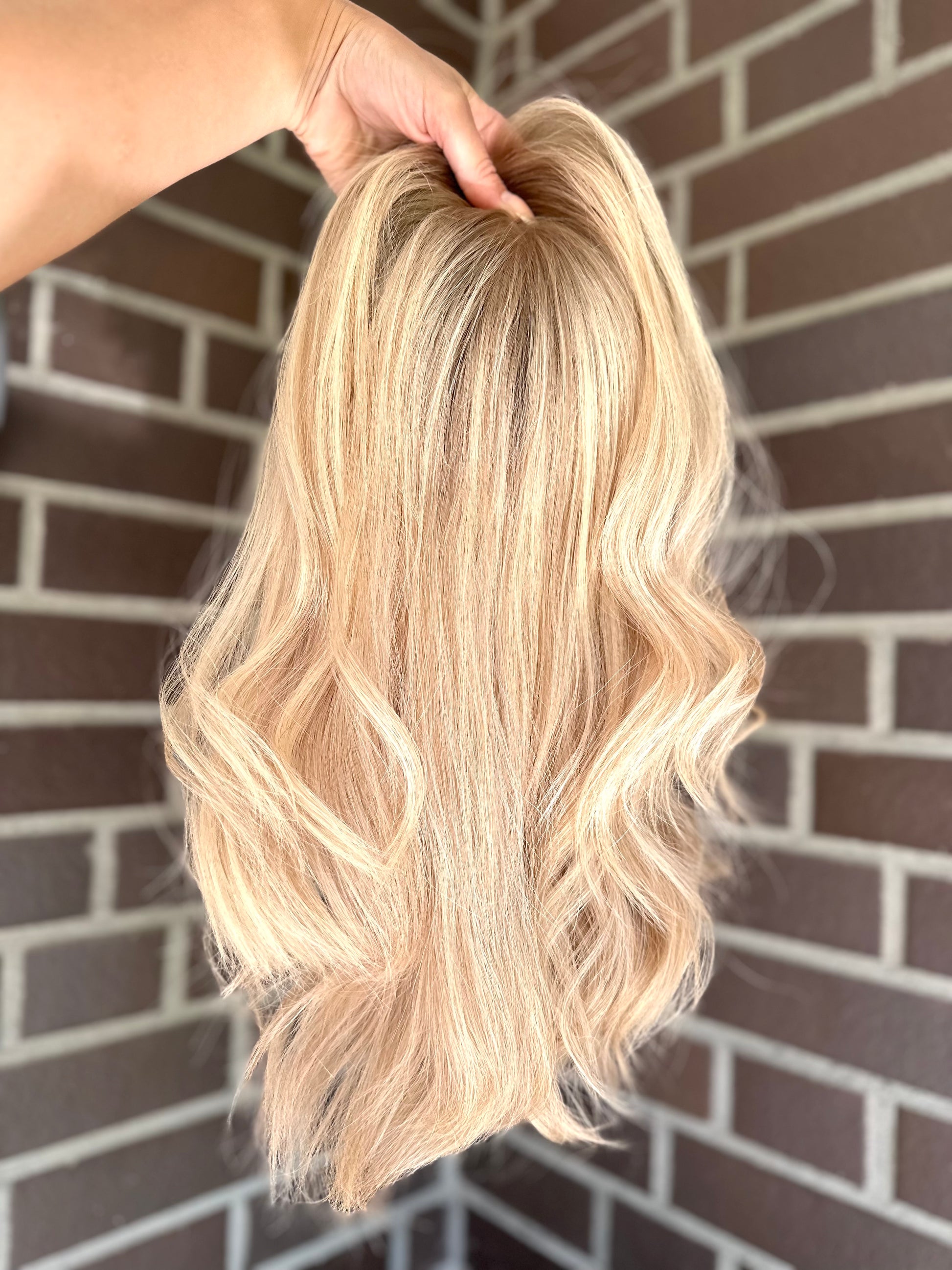 Bild zeigt blondes Echthaarteil, das frontal ins Bild gehalten wird. Bild dient der Produktpräsentation eines Artikels in der Kategorie Topper/Perücken.