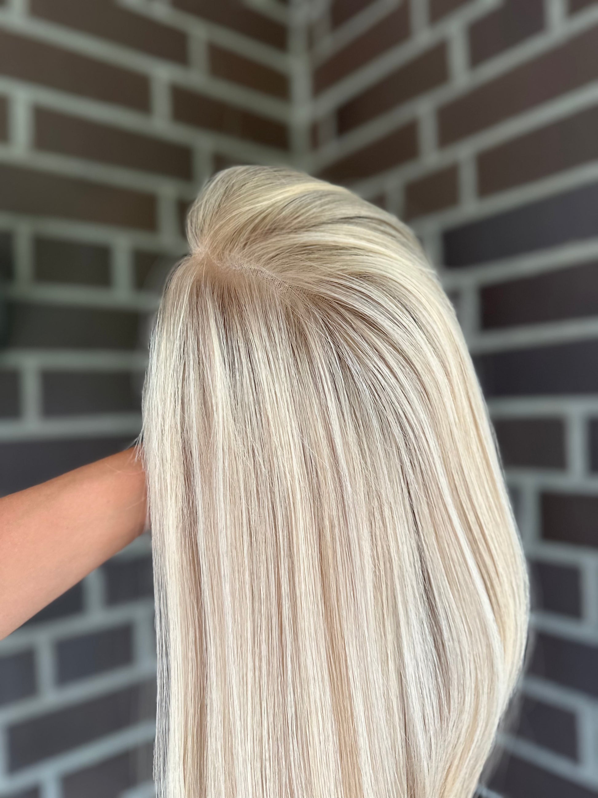 Bild zeigt blondes Echthaarteil, das seitlich ins Bild gehalten wird. Bild dient der Produktpräsentation eines Artikels in der Kategorie Topper/Perücken.