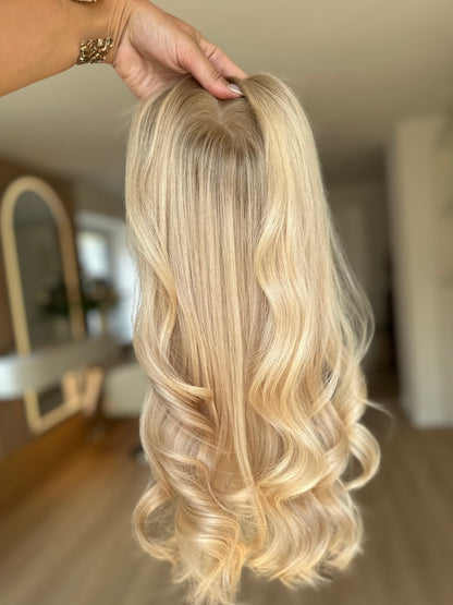 Bild zeigt blondes Echthaarteil, das frontal ins Bild gehalten wird. Bild dient der Produktpräsentation eines Artikels in der Kategorie Topper/Perücken.