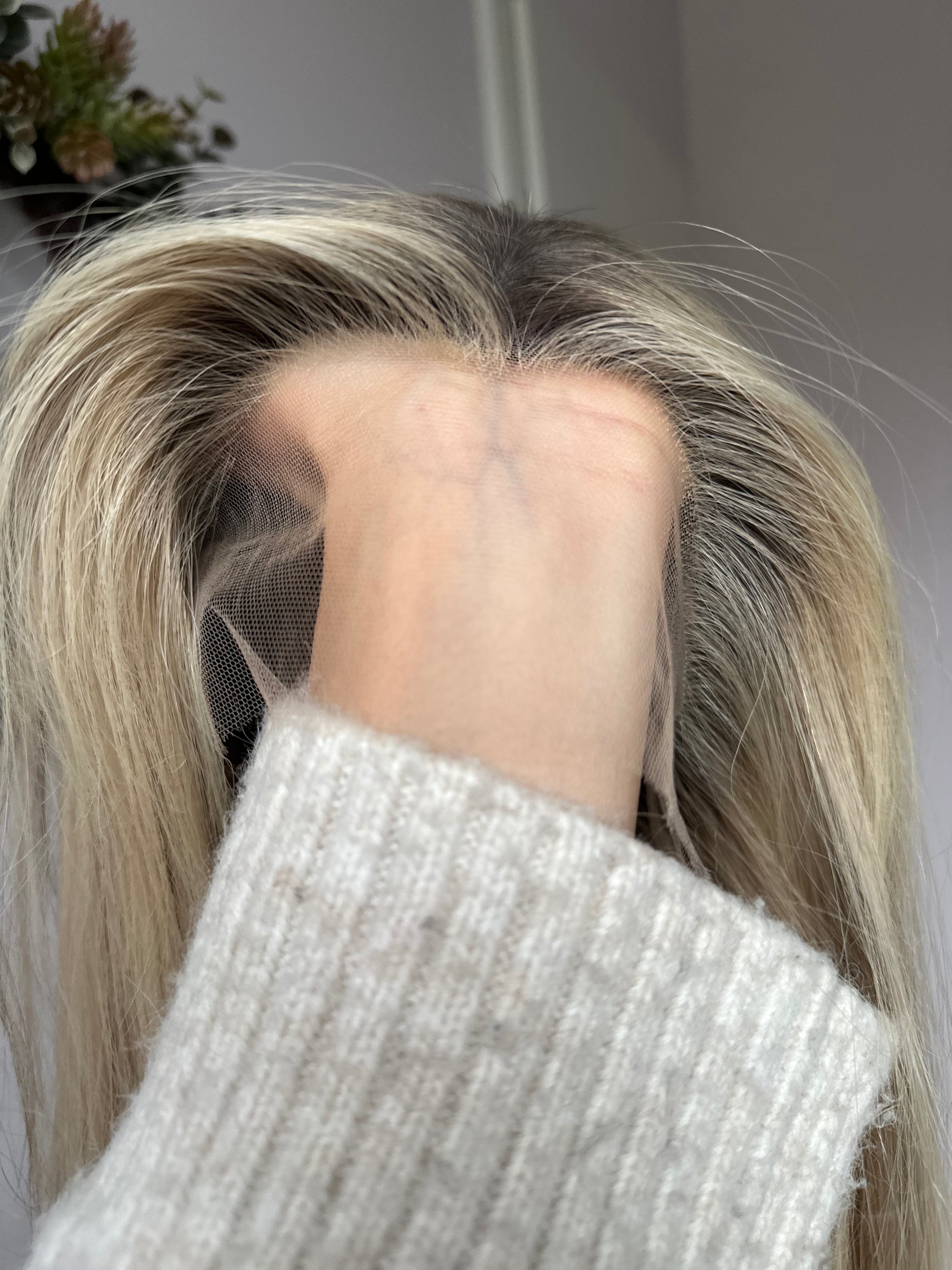 Bild zeigt blondes Echthaarteil, dessen Haaransatz  ins Bild gehalten wird. Bild dient der Produktpräsentation in der Kategorie Topper/Perücken.