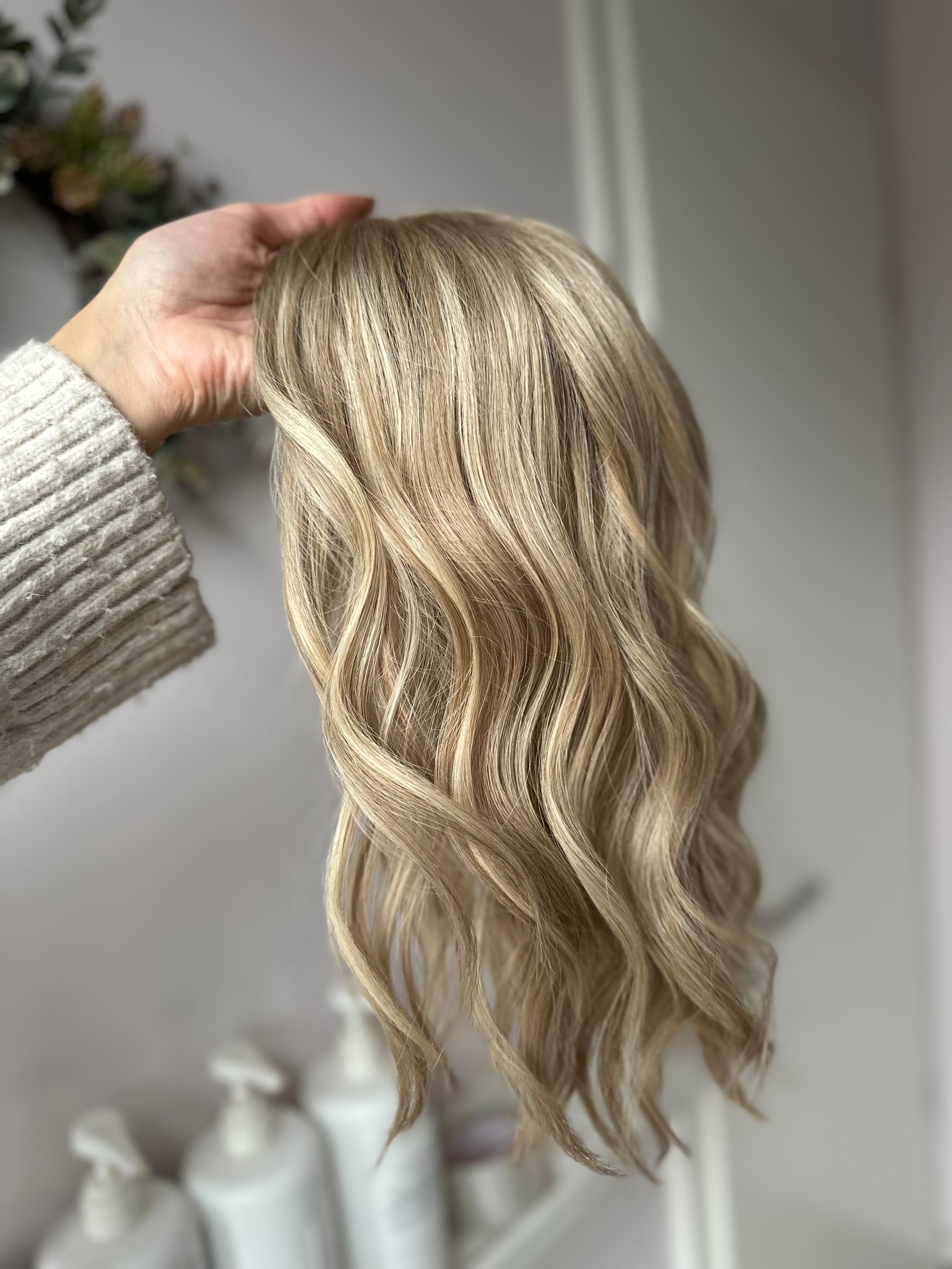 Bild zeigt blondes Echthaarteil, das seitlich ins Bild gehalten wird. Bild dient der Produktpräsentation eines Artikels in der Kategorie Topper/Perücken.