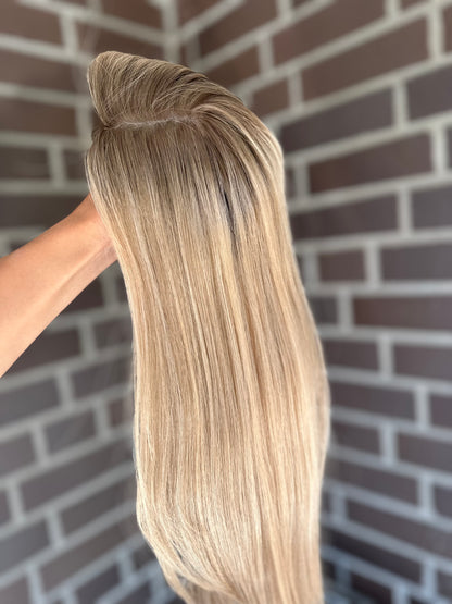 Bild zeigt blondes Echthaarteil, das seitlich ins Bild gehalten wird. Bild dient der Produktpräsentation eines Artikels in der Kategorie Topper/Perücken.