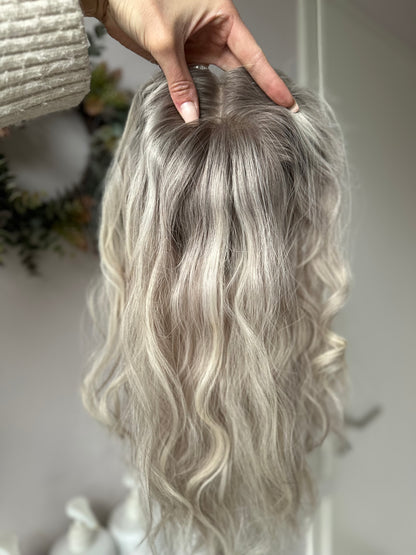 Bild zeigt blondes Echthaarteil, das frontal ins Bild gehalten wird. Bild dient der Produktpräsentation eines Artikels in der Kategorie Topper/Perücken.