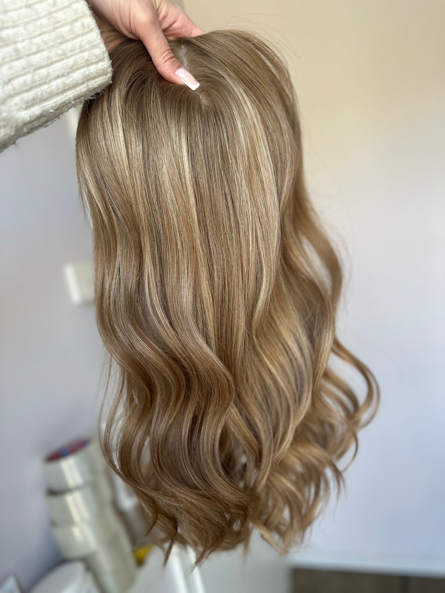 Bild zeigt blondes Echthaarteil, das frontal ins Bild gehalten wird. Bild dient der Produktpräsentation eines Artikels in der Kategorie Topper/Perücken.