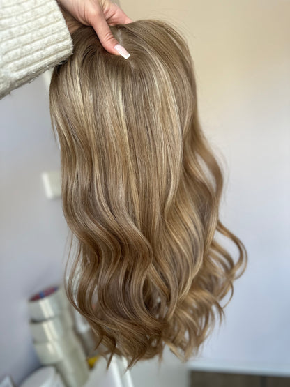 Bild zeigt blondes Echthaarteil, das frontal ins Bild gehalten wird. Bild dient der Produktpräsentation eines Artikels in der Kategorie Topper/Perücken.