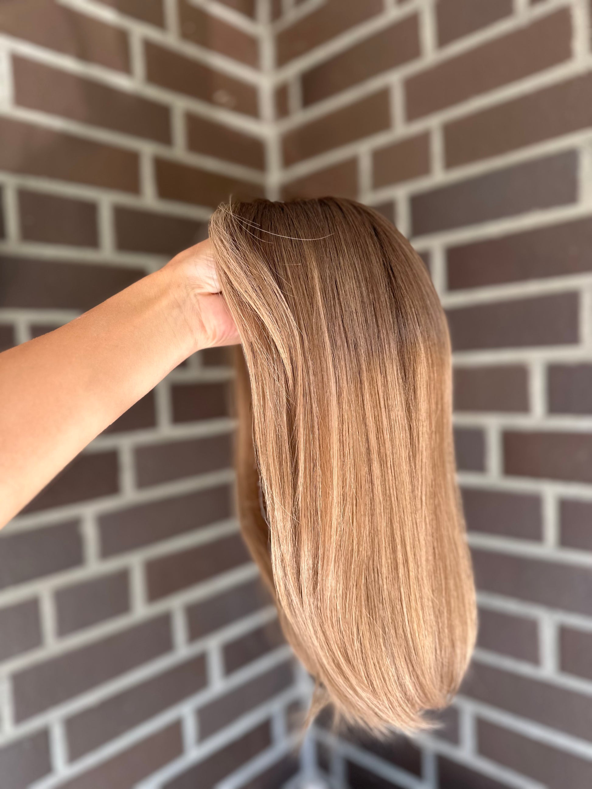 Bild zeigt blondes Echthaarteil, das seitlich ins Bild gehalten wird. Bild dient der Produktpräsentation eines Artikels in der Kategorie Topper/Perücken.