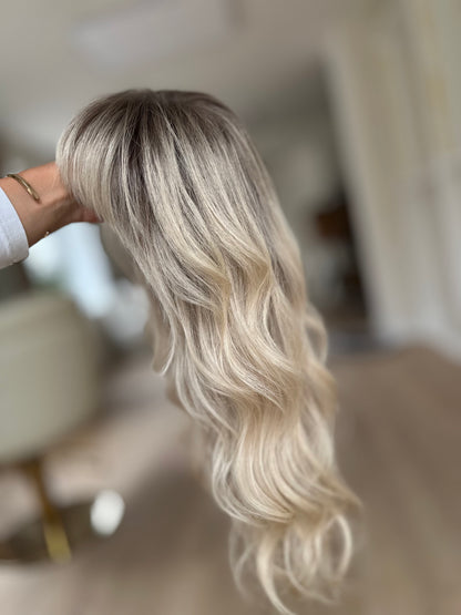 Bild zeigt blondes Echthaarteil, das seitlich ins Bild gehalten wird. Bild dient der Produktpräsentation eines Artikels in der Kategorie Topper/Perücken.