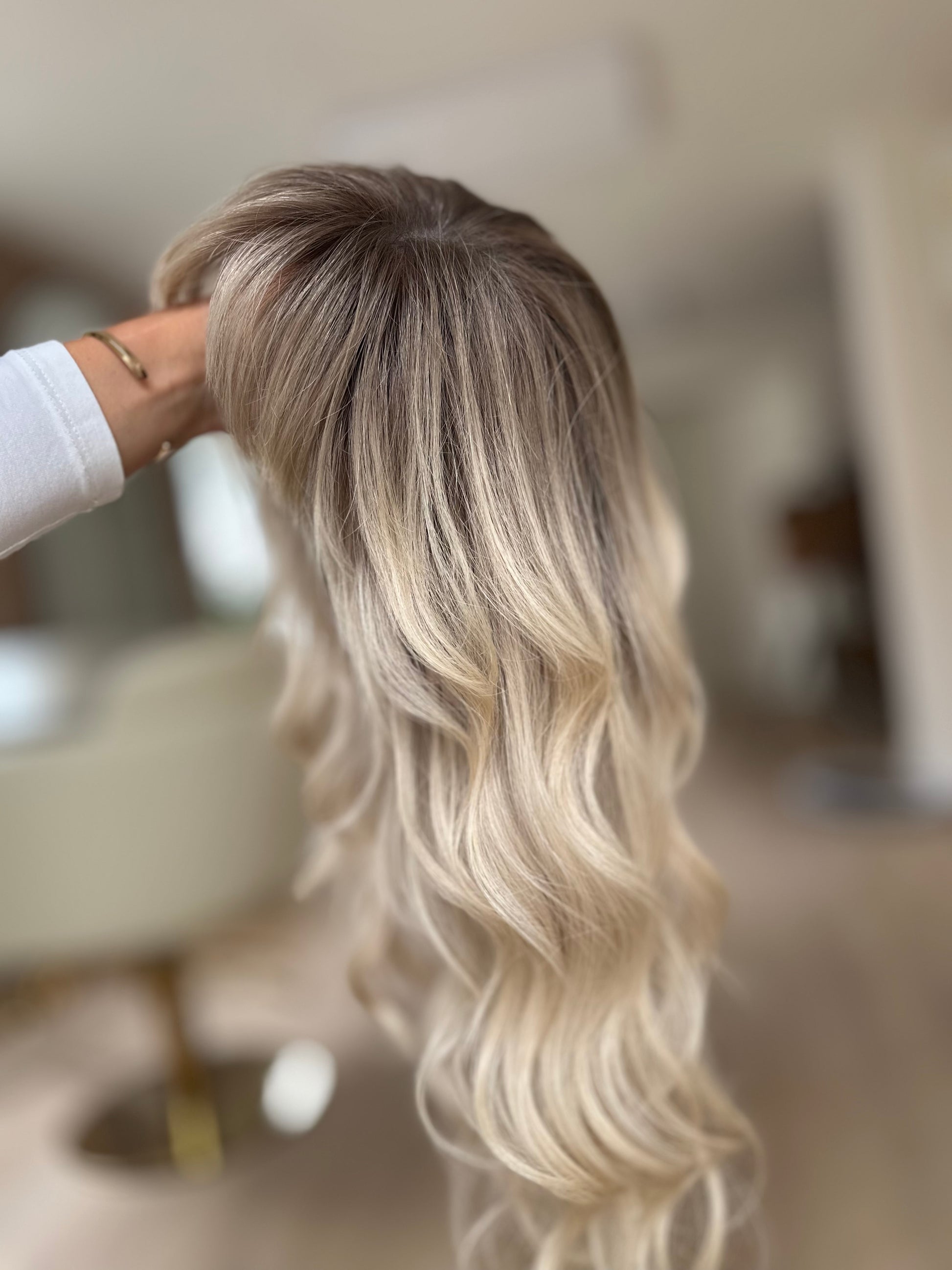 Bild zeigt blondes Echthaarteil, das seitlich ins Bild gehalten wird. Bild dient der Produktpräsentation eines Artikels in der Kategorie Topper/Perücken.