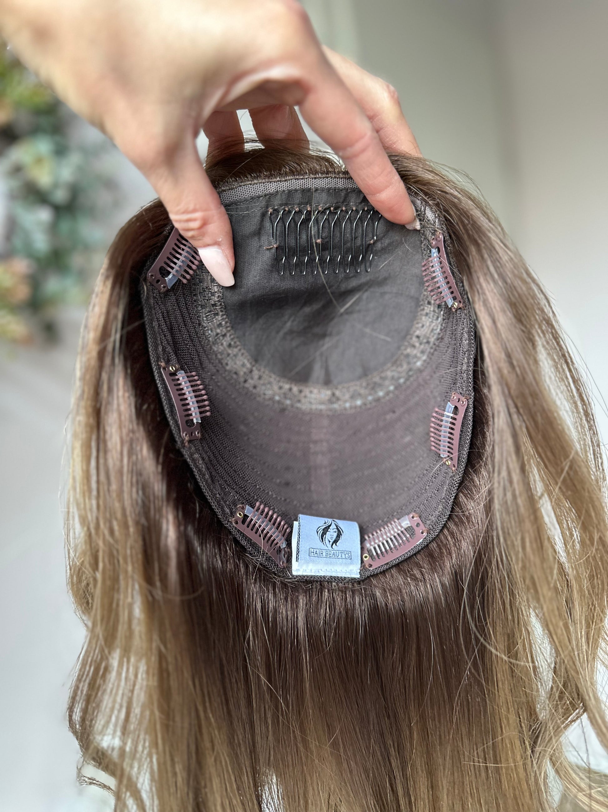 Bild zeigt blondes Echthaarteil, das frontal ins Bild gehalten wird. Bild dient der Produktpräsentation eines Artikels in der Kategorie Topper/Perücken.