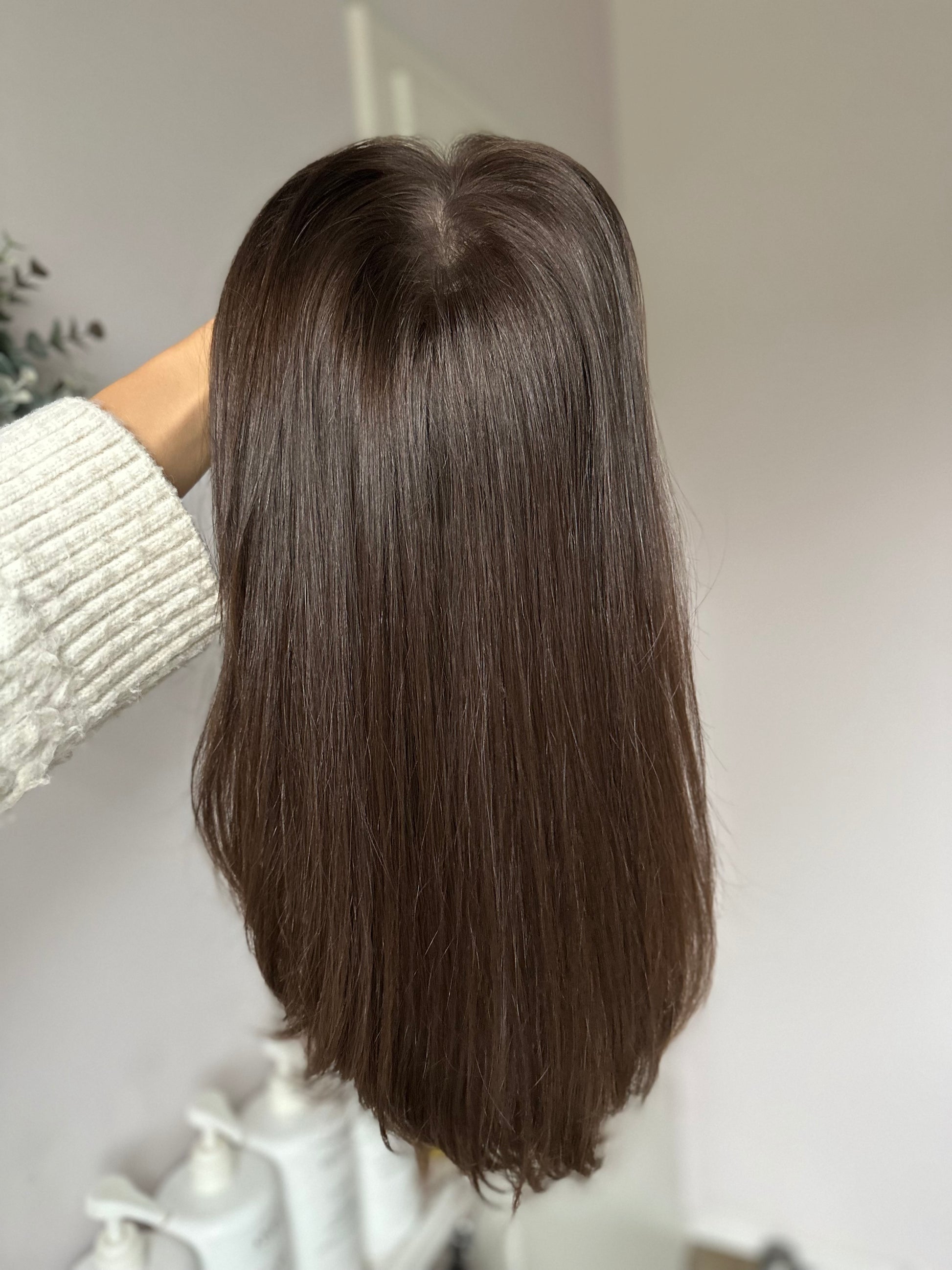 Bild zeigt braunes Echthaarteil, das frontal ins Bild gehalten wird. Bild dient der Produktpräsentation eines Artikels  in der Kategorie Topper/Perücken.