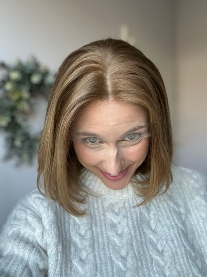 Bild zeigt attraktive Frau, die ihren Kopf leicht beugt, sodass blonder Haaransatz sichtbar wird. Bild dient der Produktpräsentation eines Artikels in der Kategorie Topper/Perücken.