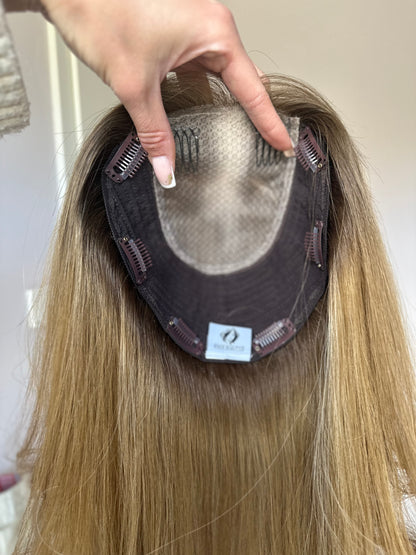 Bild zeigt blondes Echthaarteil, das frontal ins Bild gehalten wird. Bild dient der Produktpräsentation eines Artikels in der Kategorie Topper/Perücken.