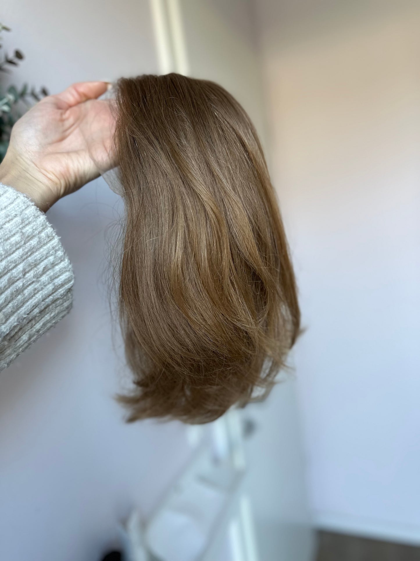 Bild zeigt blondes Echthaarteil, das seitlich ins Bild gehalten wird. Bild dient der Produktpräsentation eines Artikels in der Kategorie Topper/Perücken.